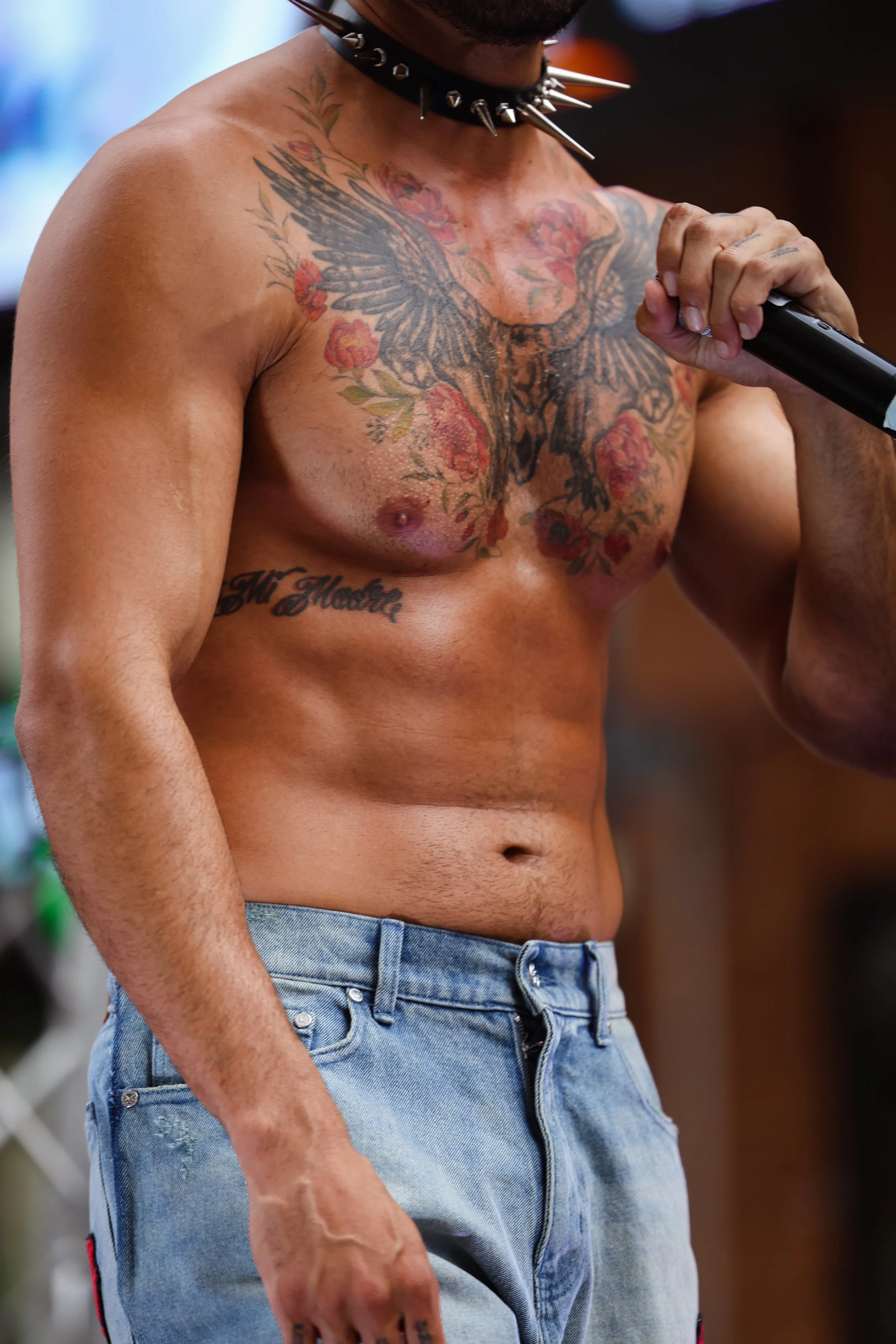 A shirtless man with tattoos holding a microphone.