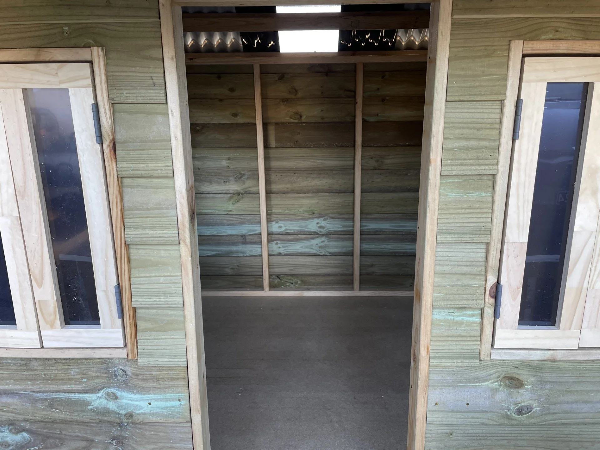 A partially built wooden structure with an open doorway, showing the interior framing and special windows on either side.