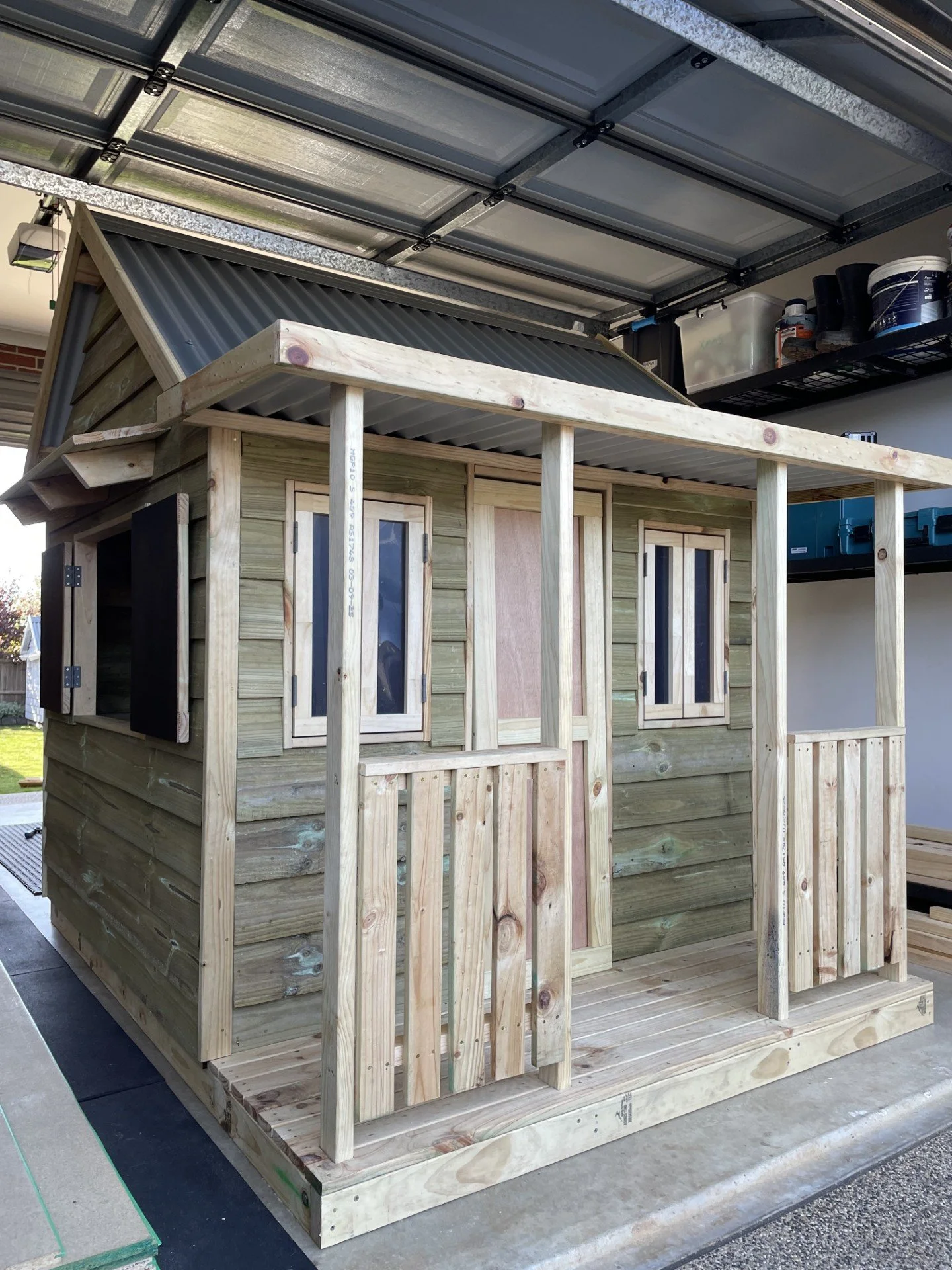 Unfinished small wooden playhouse under construction, with a roof frame and walls, set in a garage or workshop.