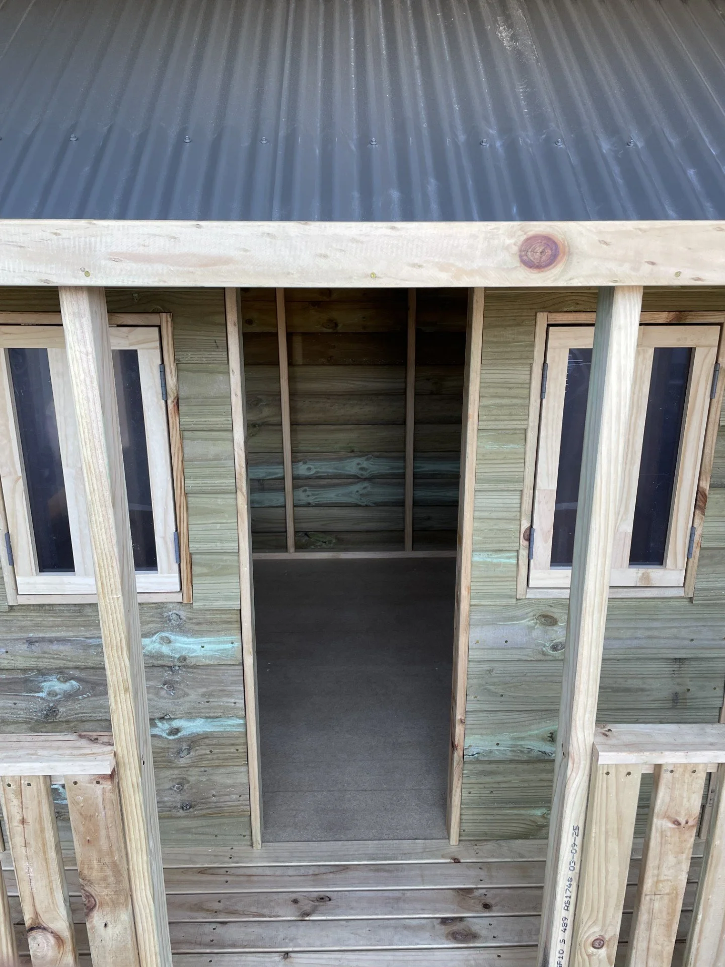 Construction of a small wooden shed with a metal roof, showing framing and window openings