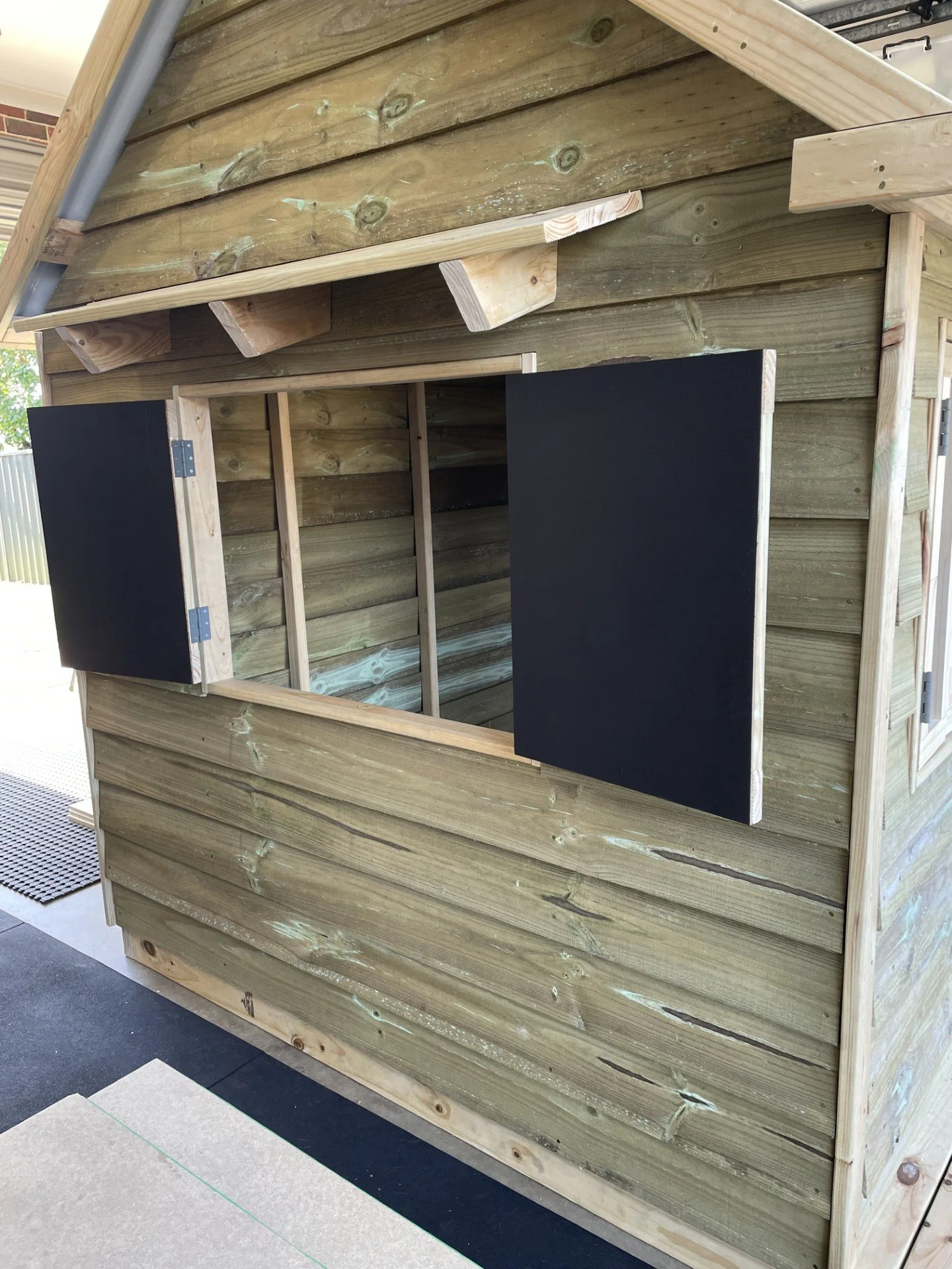 Wooden playhouse with open window shutters and a sloped roof, situated indoors.