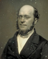 A black and white photograph of a man with glasses, wearing a suit and bow tie.
