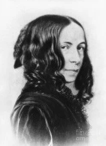 Thoughts on the spiritual world. A black and white portrait of a woman with wavy shoulder-length hair, turning slightly to the right, with a neutral expression.