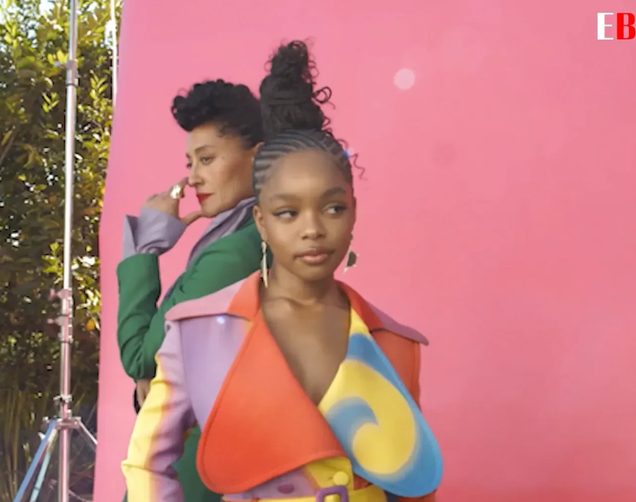 Two models in colorful looks against a pink backdrop
