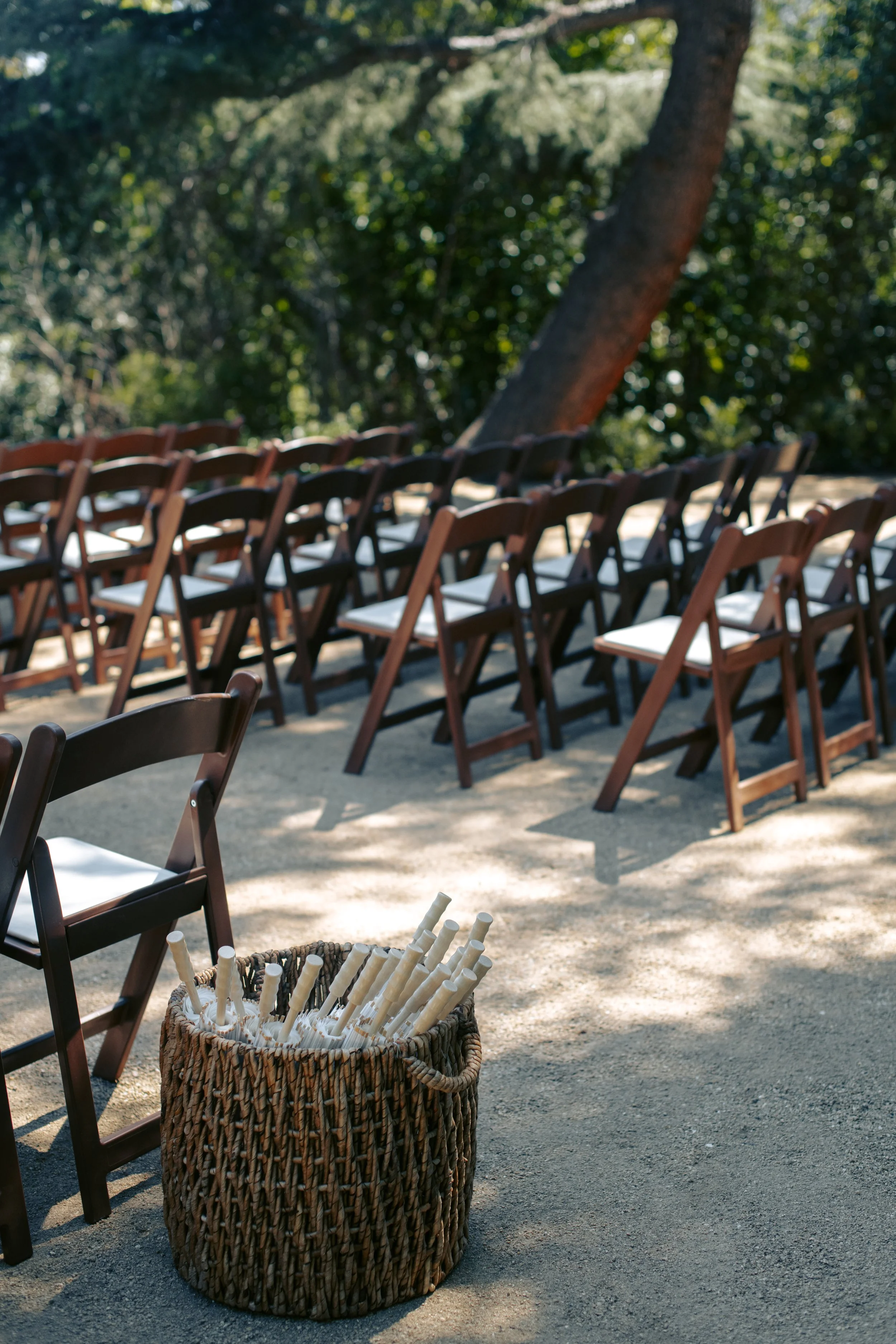 Rows of wooden folding chairs set for a garden ceremony, a woven basket at the aisle