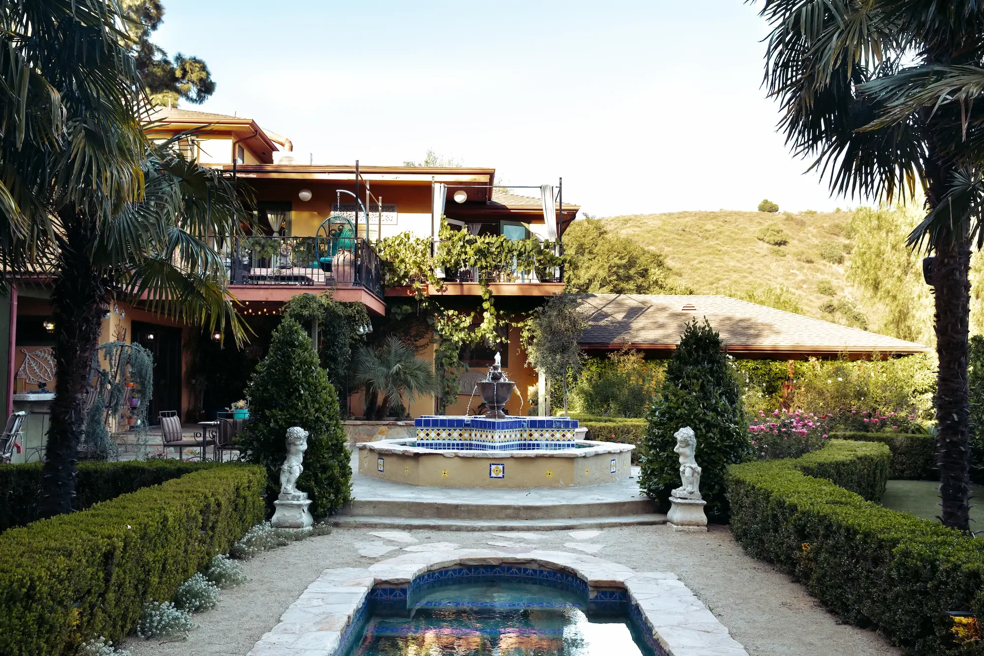 View across the pool toward the built-in fountain, landscaped garden, and rolling Hollywood Hills.