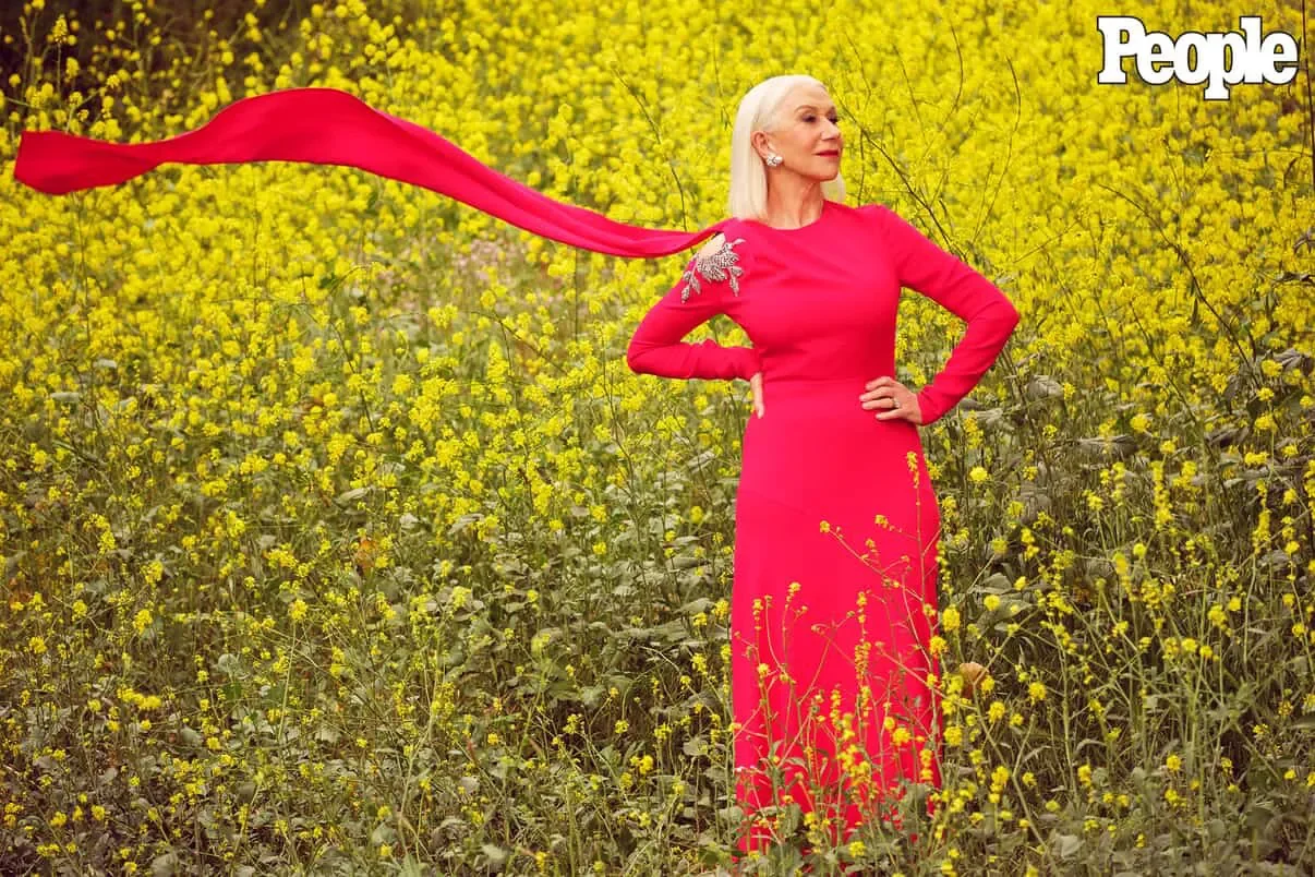 Model in a red gown with a flowing scarf posing in a field of golden wildflowers