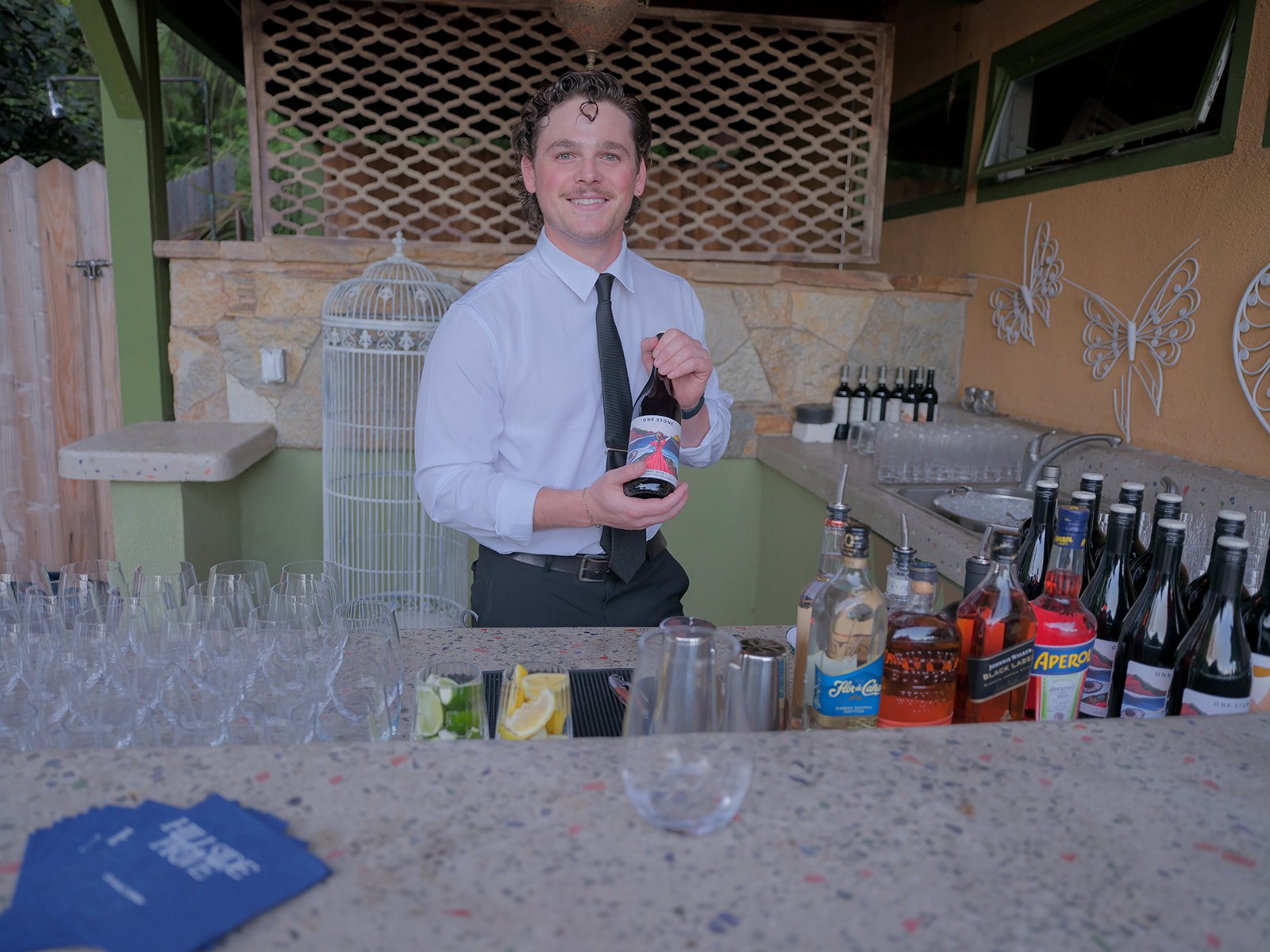 Bartender preparing drinks at an outdoor bar lined with bottles