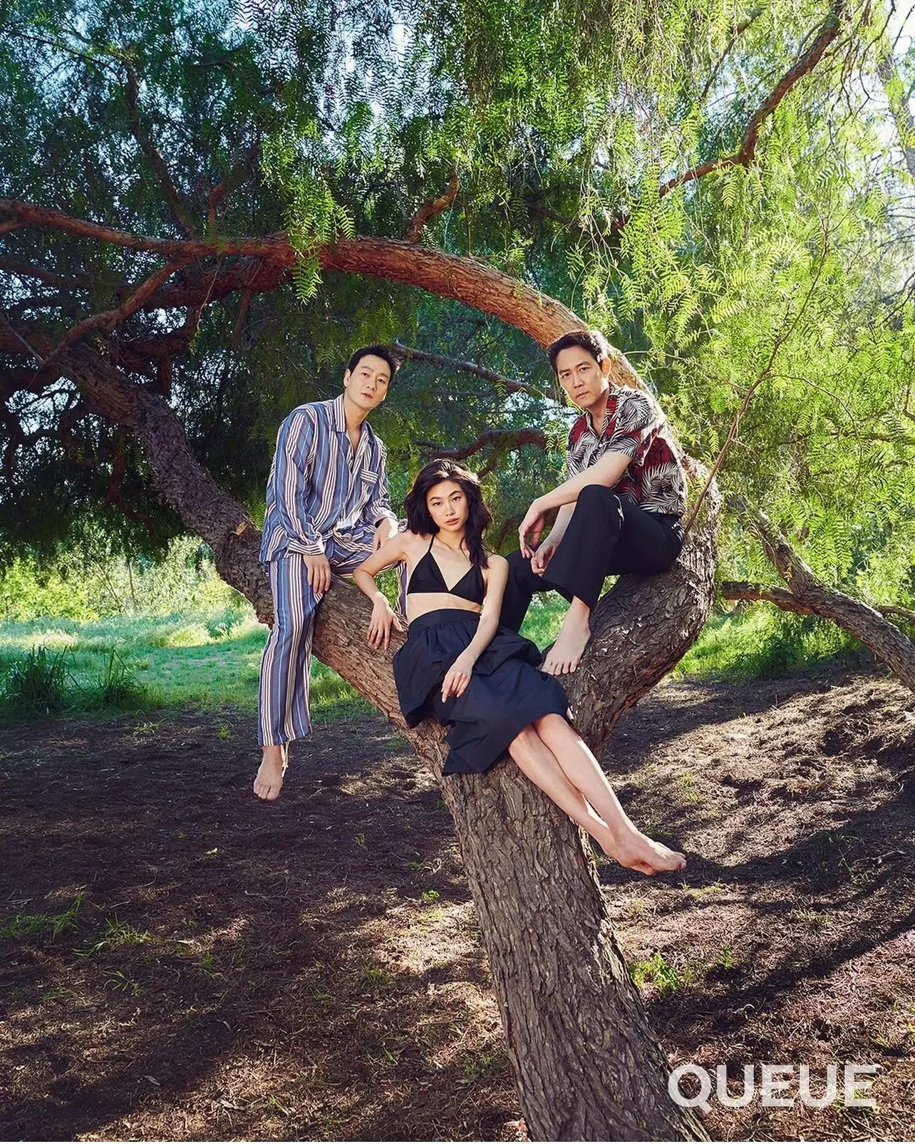 Three models in coordinated looks posing on and around a garden tree