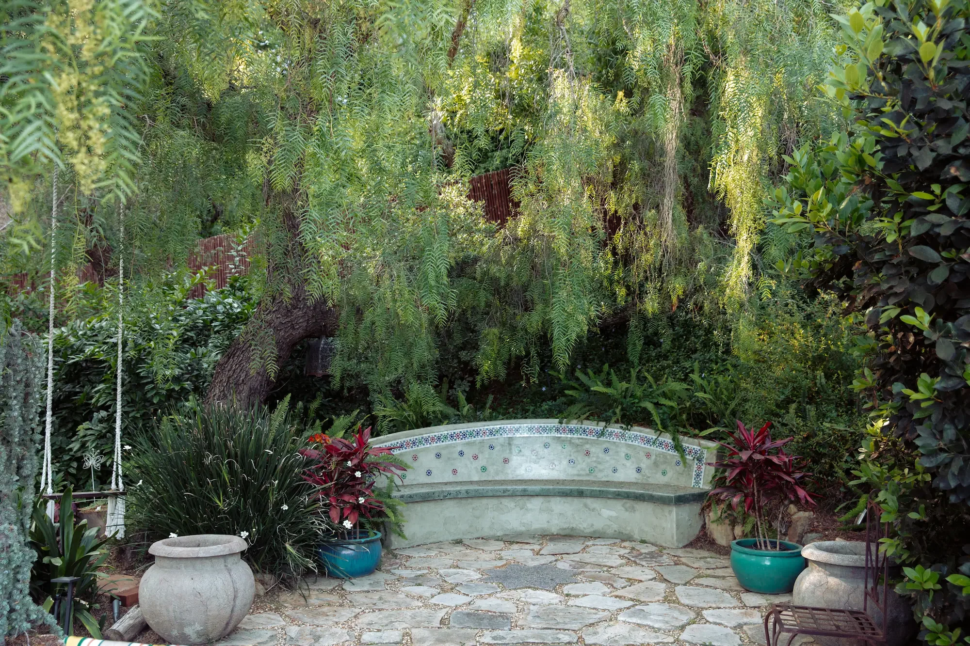 Lush garden setting at XOHH Events featuring a handcrafted Moroccan bench finished with traditional zellige tile, a decorative glass star detail on the front, and broken-pebble mosaic accents. Hanging Moroccan lanterns overhead add texture and atmosp