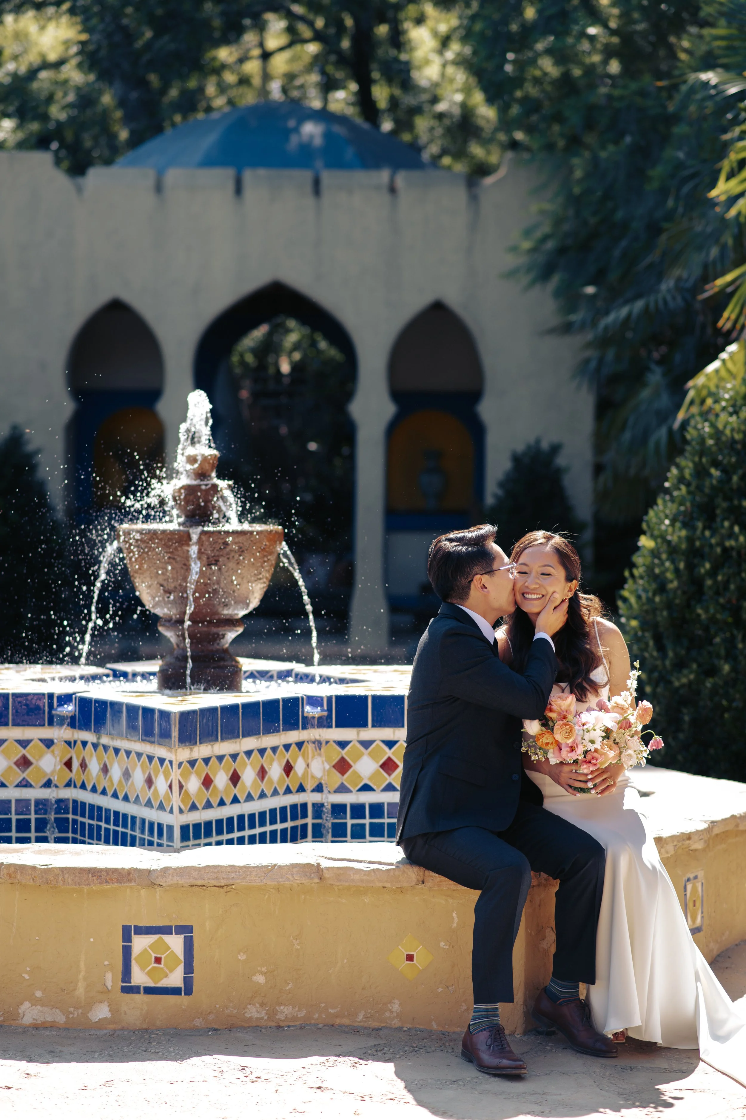 Newlyweds embracing beside the tiled Moroccan fountain as water sprays behind them