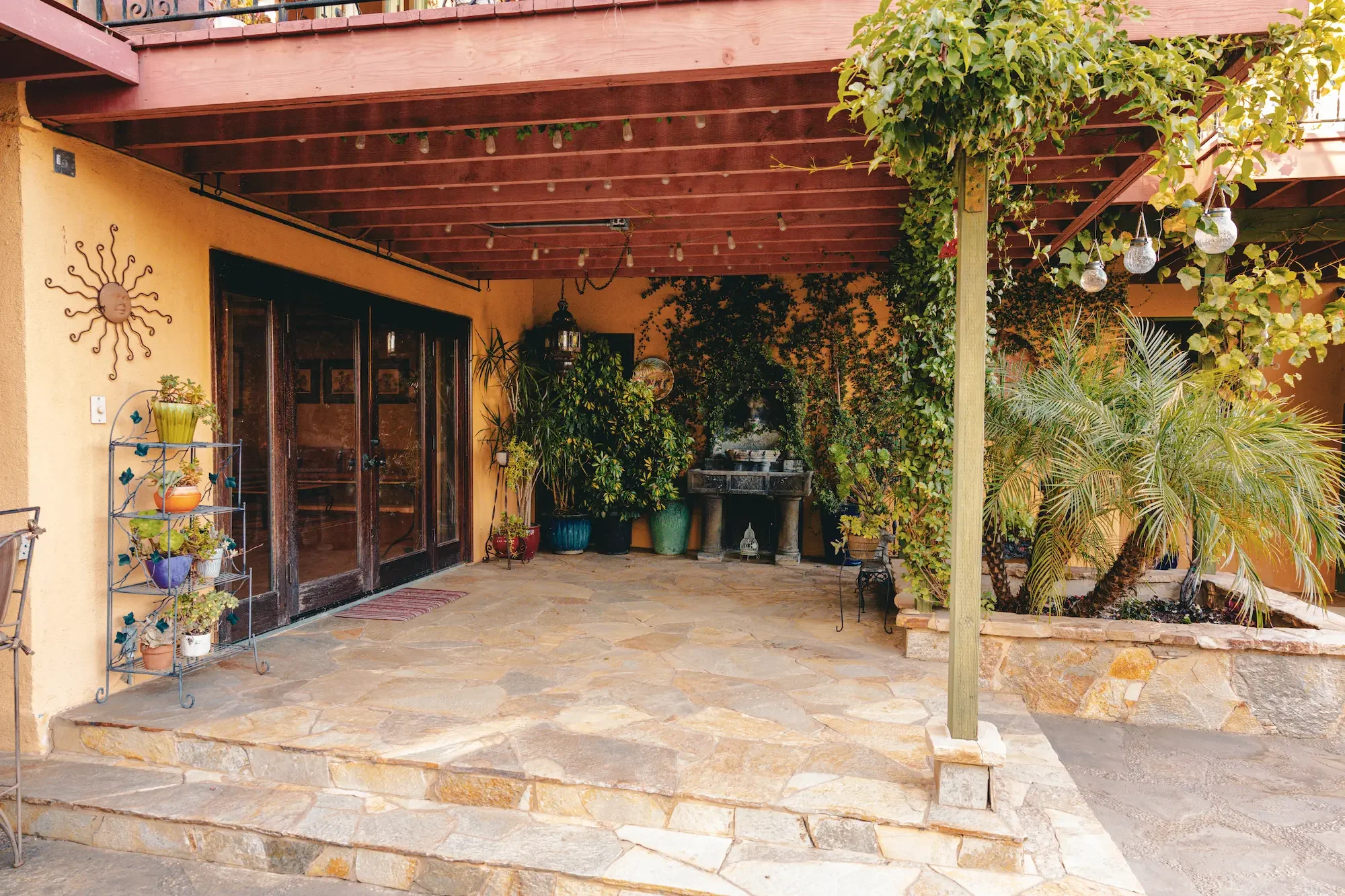 Covered stone patio featuring a built-in fountain, garden greenery, and a large Moroccan lantern.