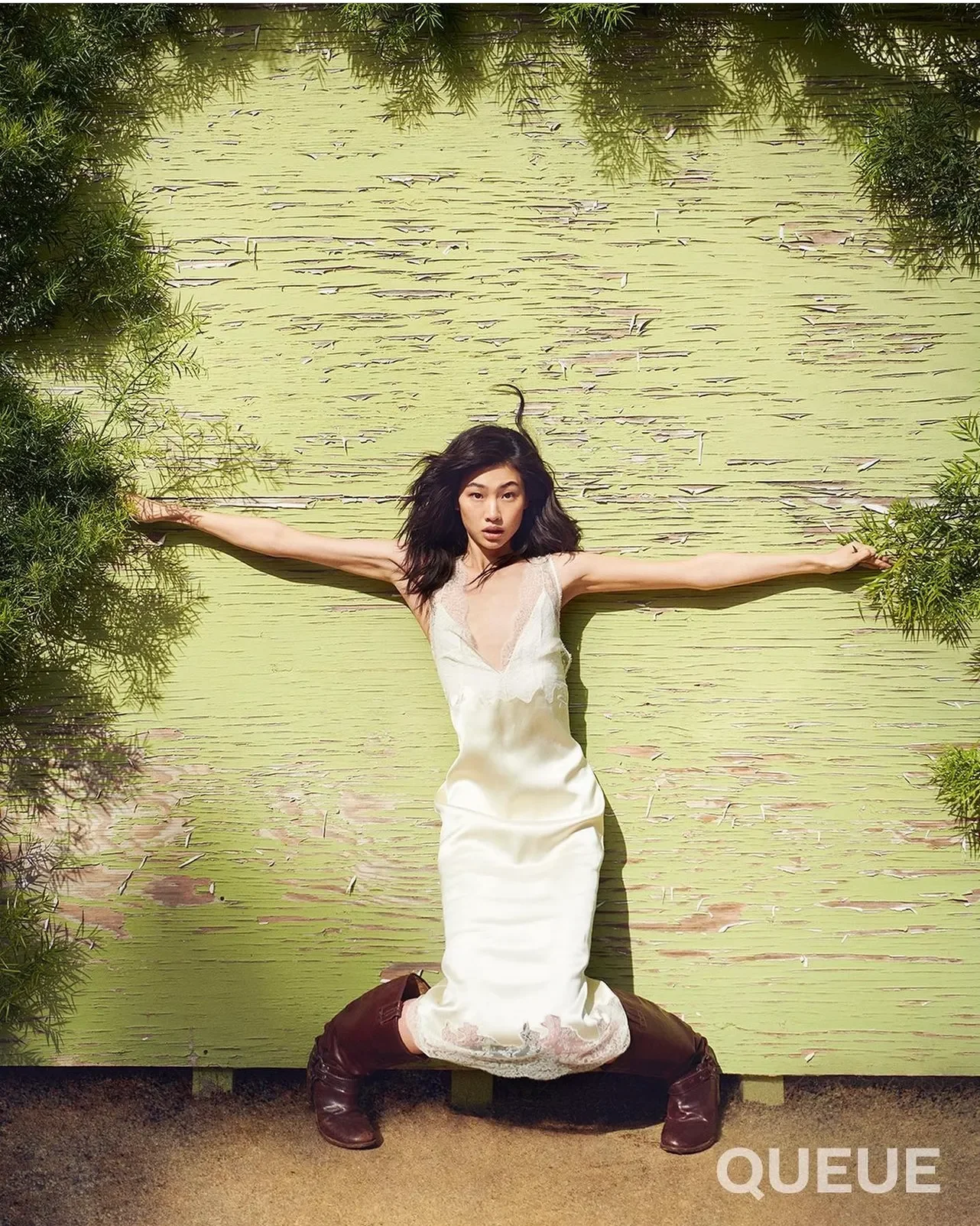 Model in a white gown on a garden swing, arms outstretched among the greenery