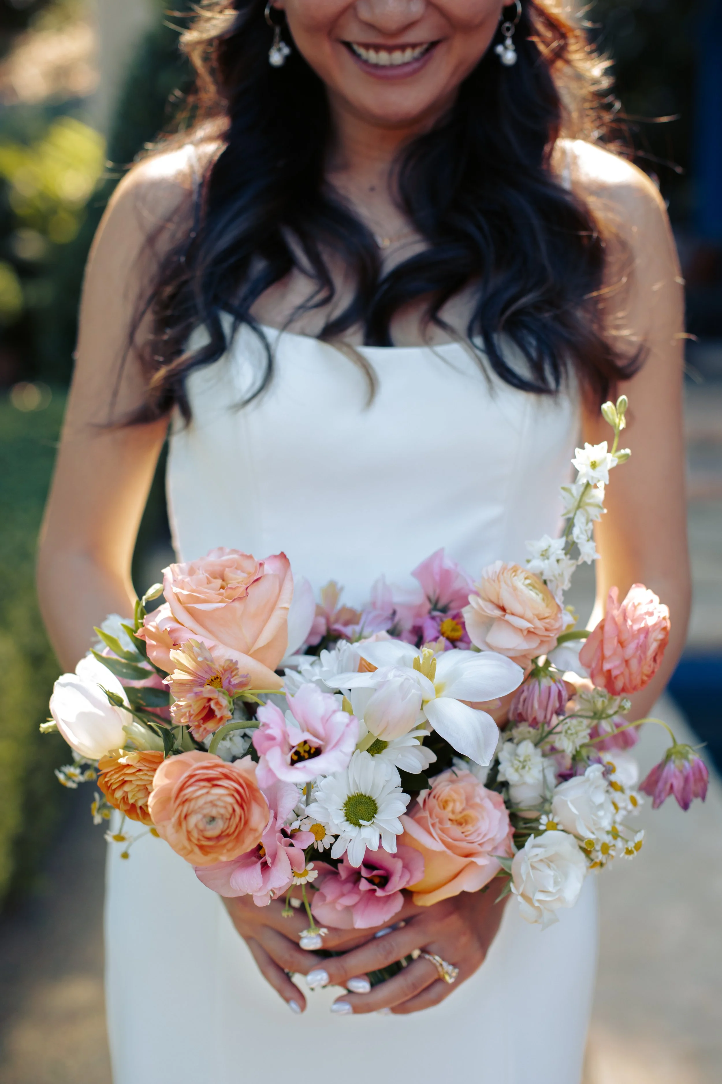 Bride holding a lush bouquet of peach, pink and white blooms against her white gown.
