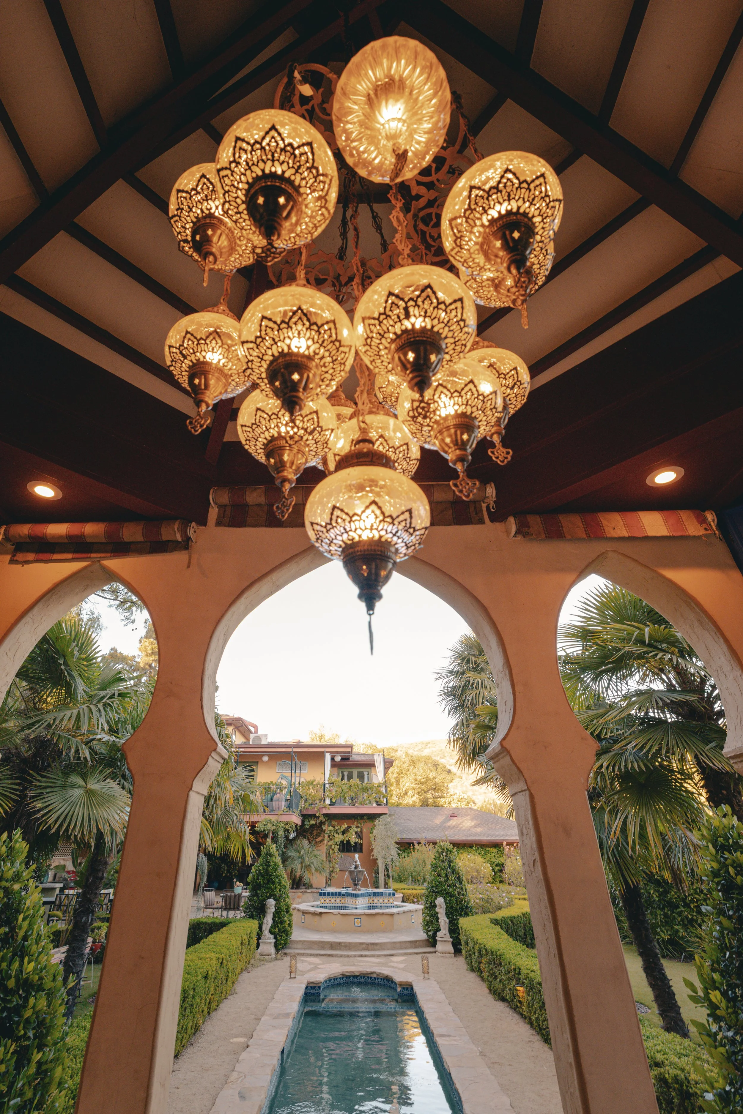 Ornate Moroccan chandeliers above a keyhole archway framing the gardens and fountain