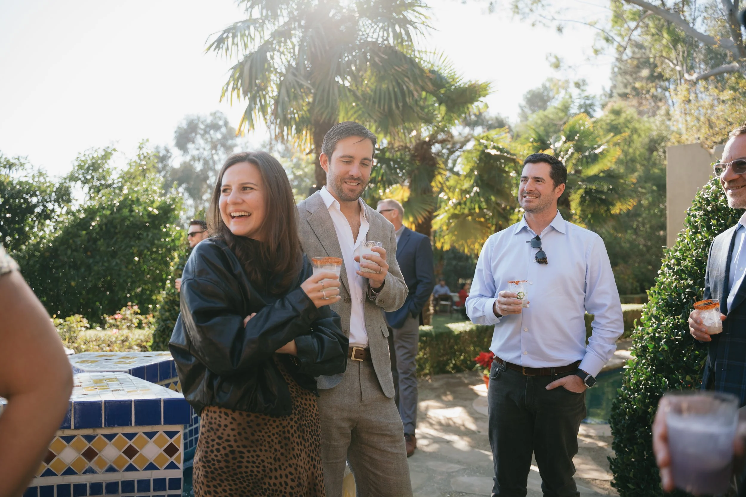 Guests laughing with cocktails in hand at an outdoor gathering among the palms.