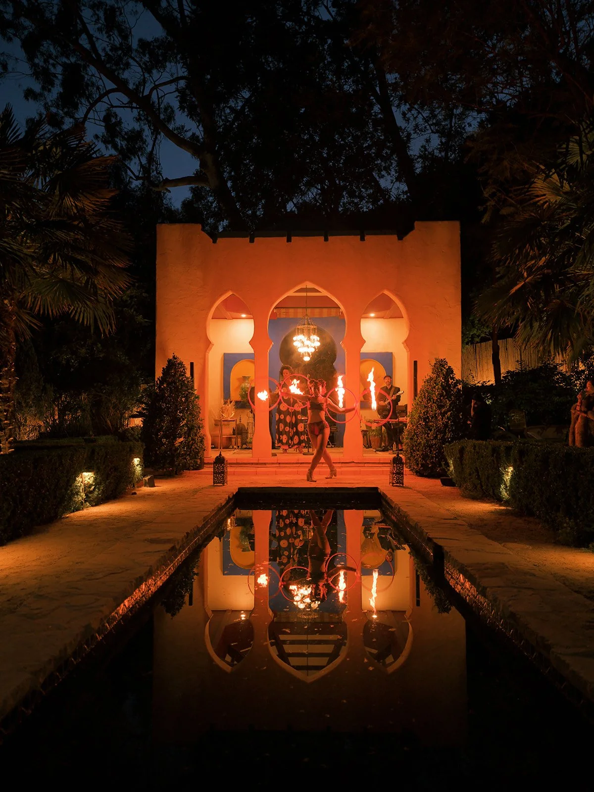 Moroccan pavilion glowing at night with a fire performer, reflected in the pool.
