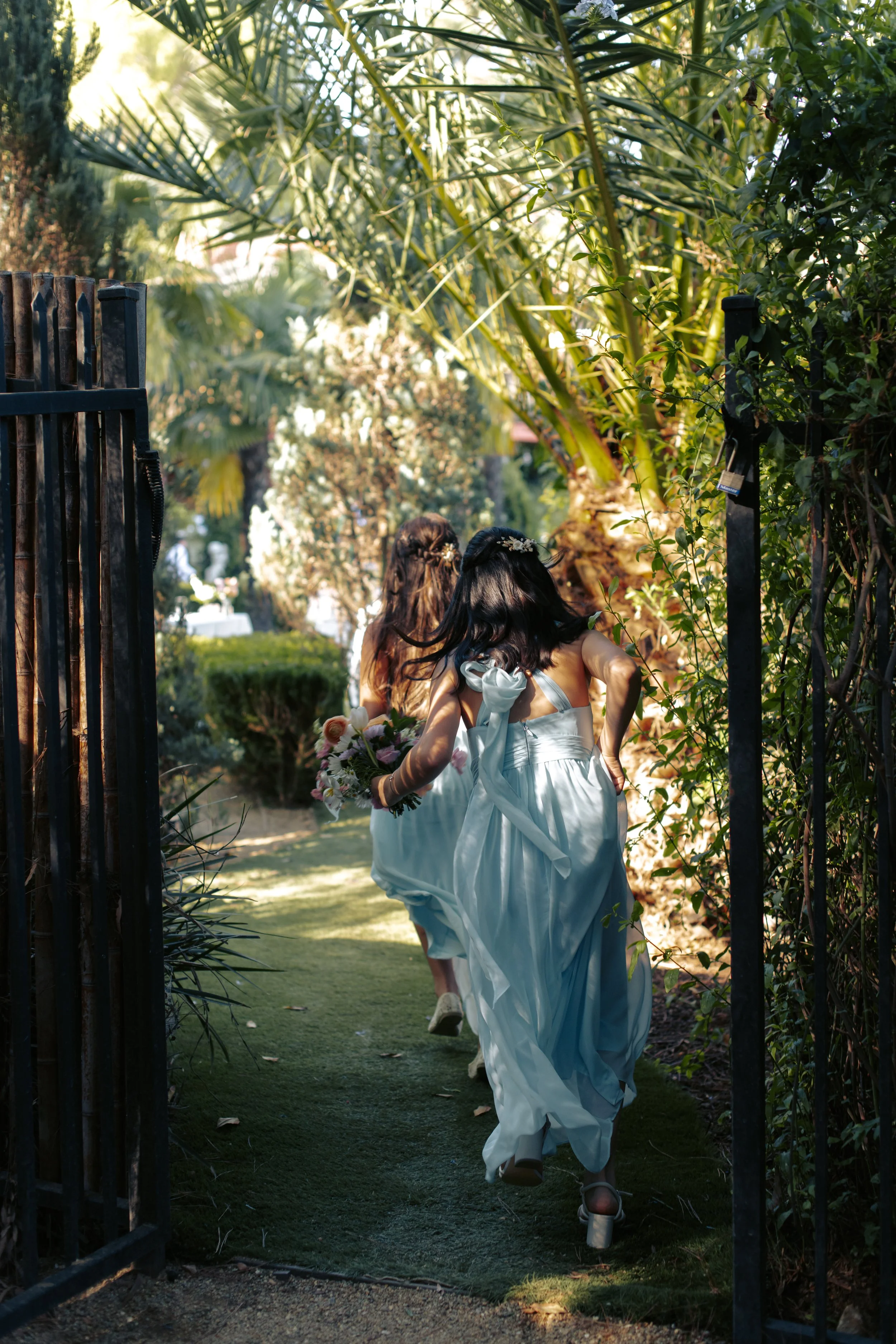 Guest in a pale blue dress walking through a wrought-iron garden gate