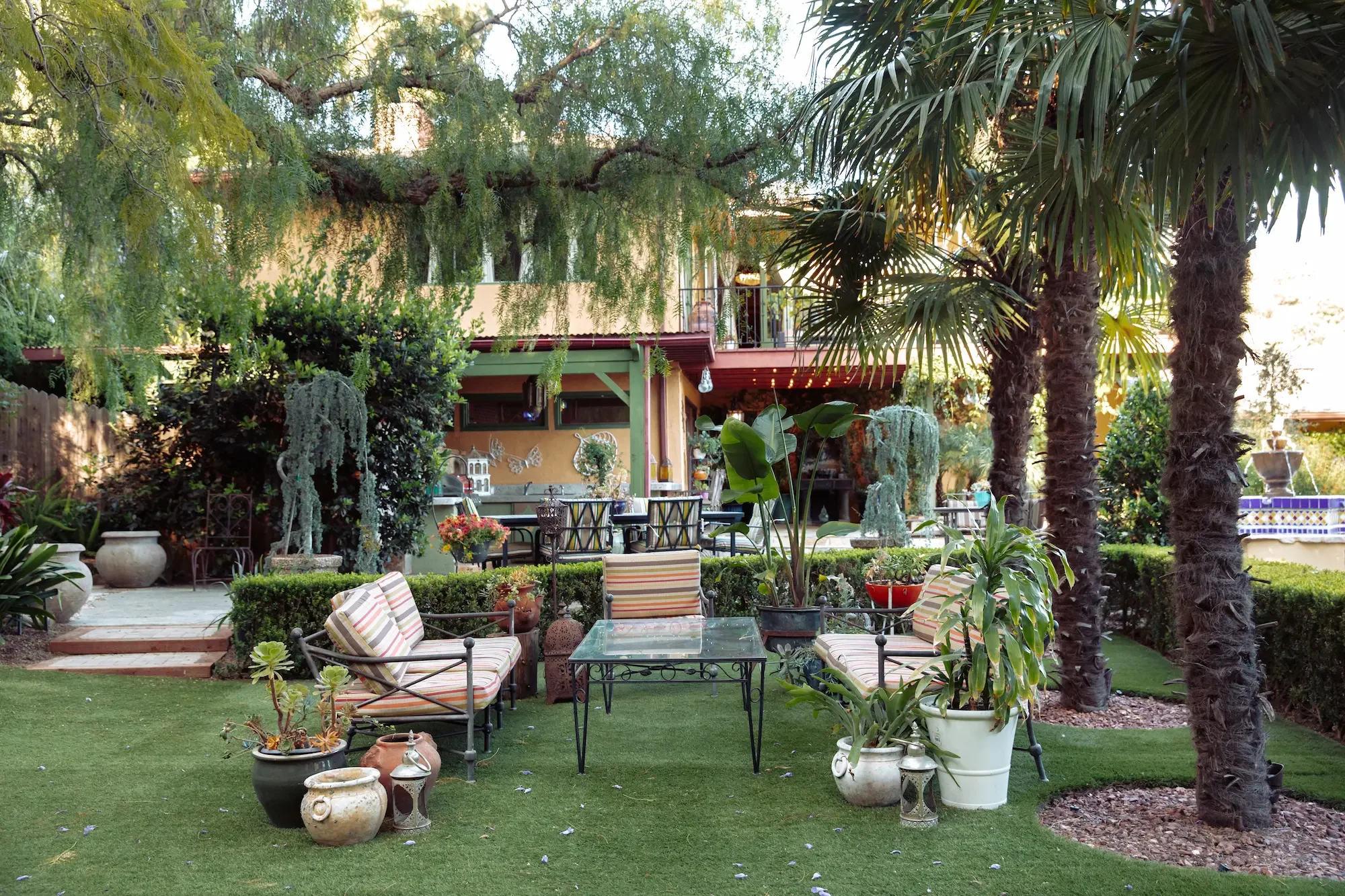 Outdoor sitting area on the open lawn, surrounded by palm trees and a mature California pepper tree.