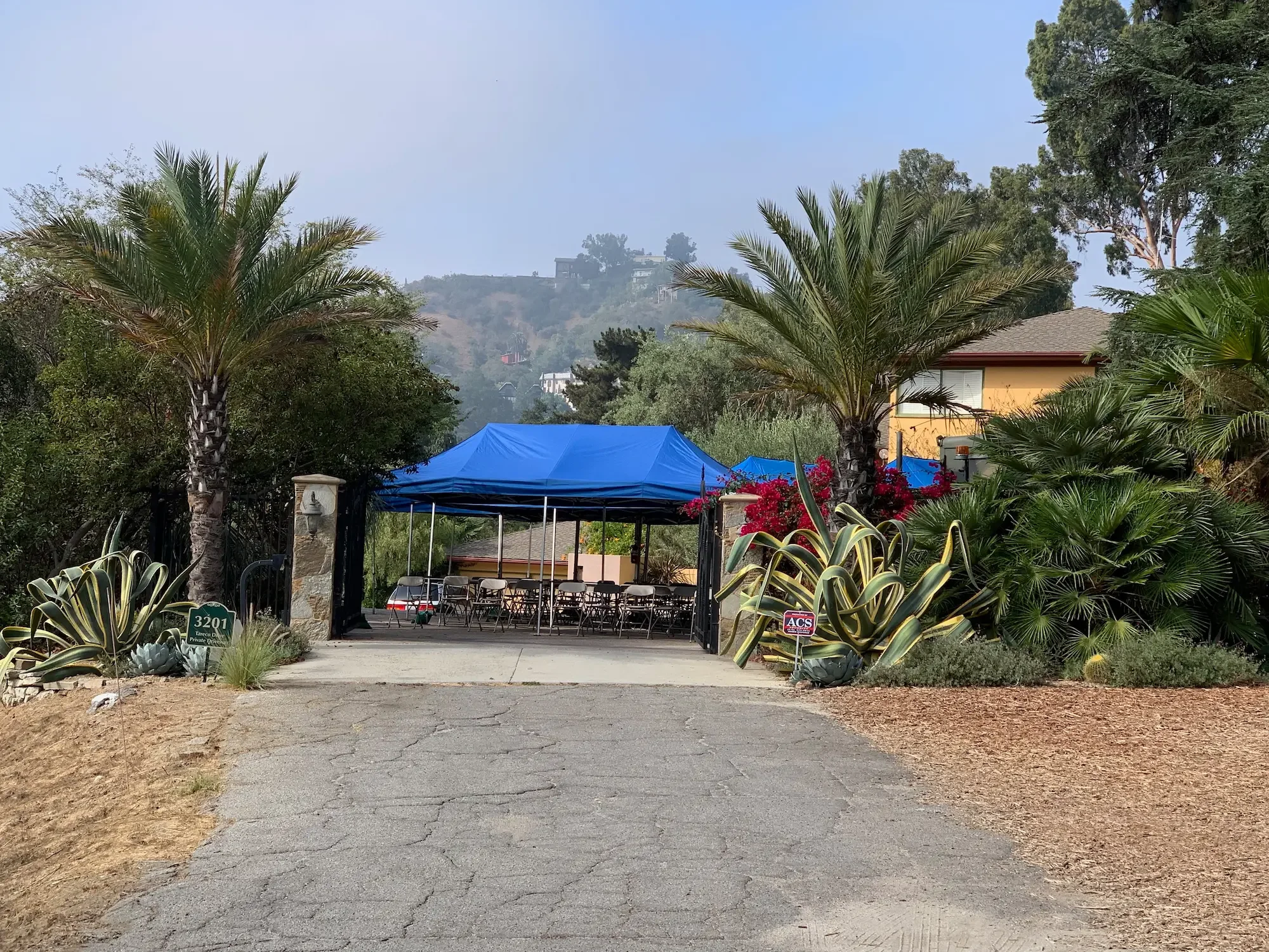 Wide view of an outdoor crew staging area with a blue canopy and surrounding gardens at XOHH Events in Los Angeles