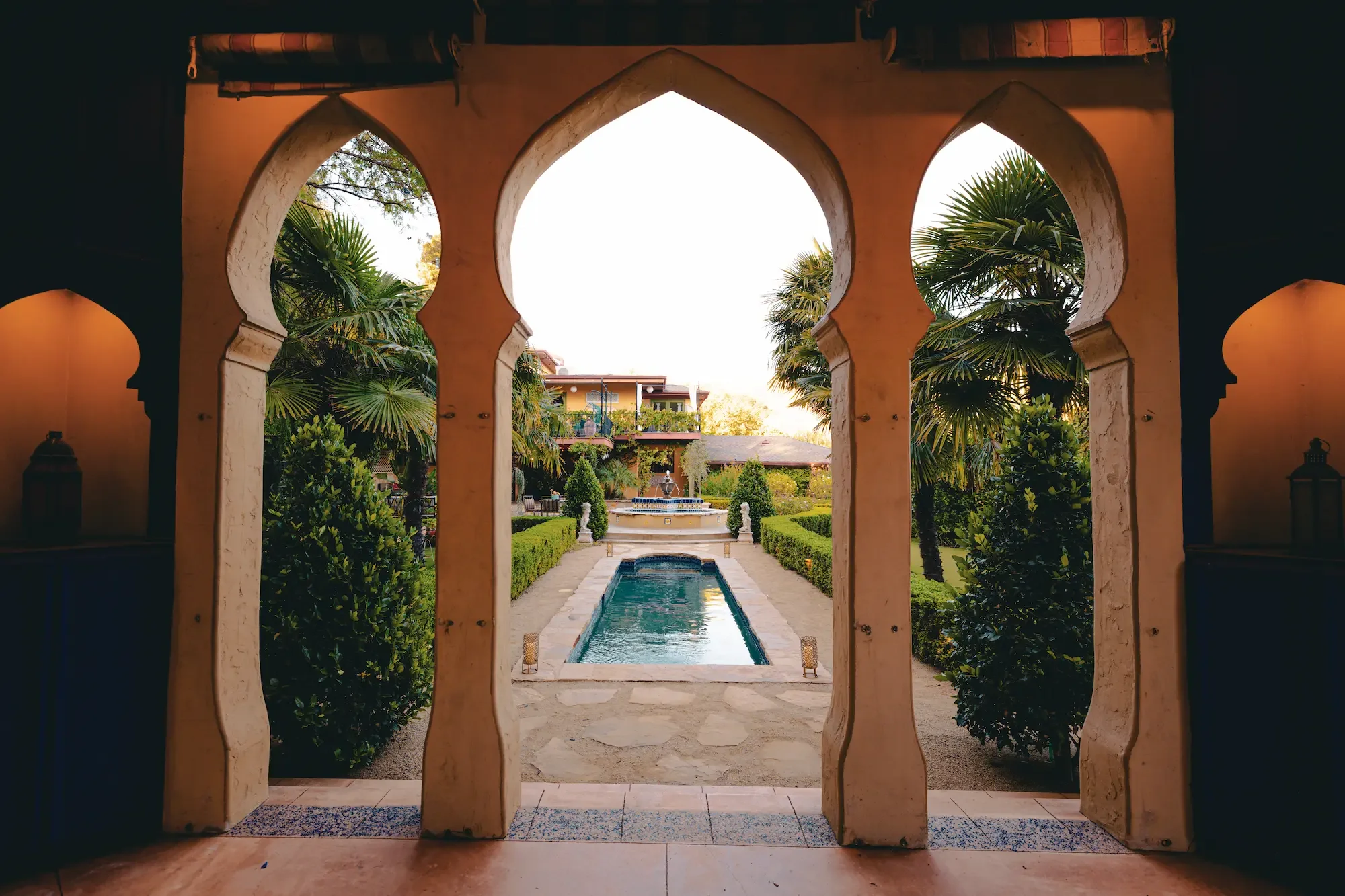 View from inside the Kasbah through three Moroccan arches toward the pool, garden paths, palms, and fountain at XOHH Events in the Hollywood Hills.