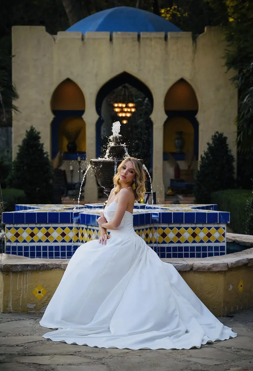Bride in a full ballgown seated on the edge of the blue-tiled estate fountain