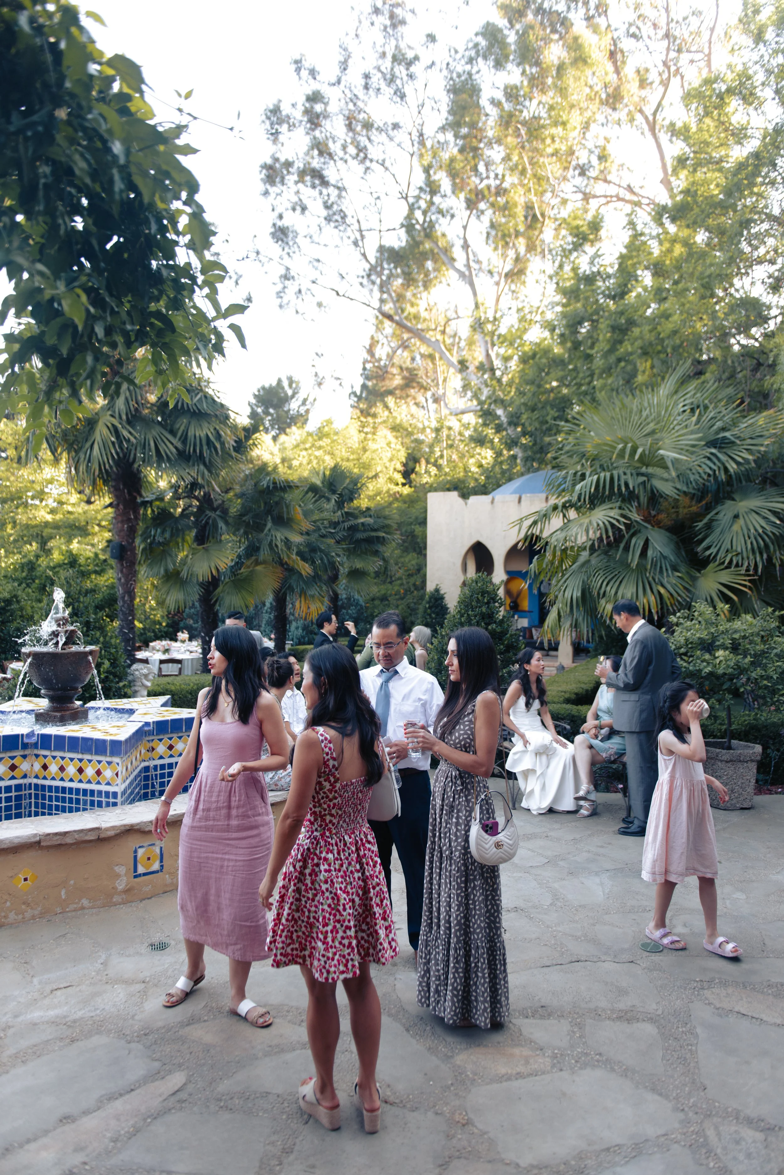 Cocktail-hour guests mingling in pastel attire beside the tiled pool