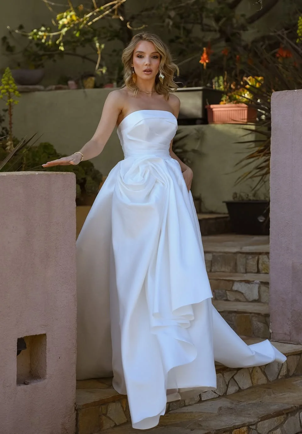 Bride in a strapless gown posing beside a warm garden wall
