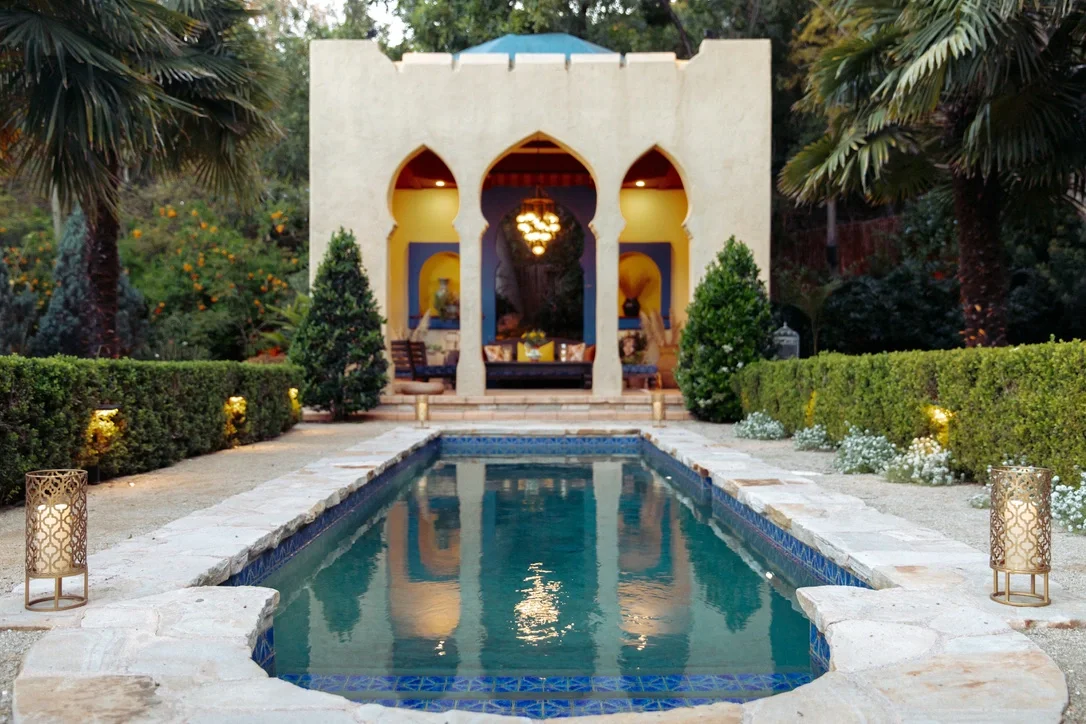 White Moroccan pavilion with keyhole arches mirrored in a long tiled reflecting pool