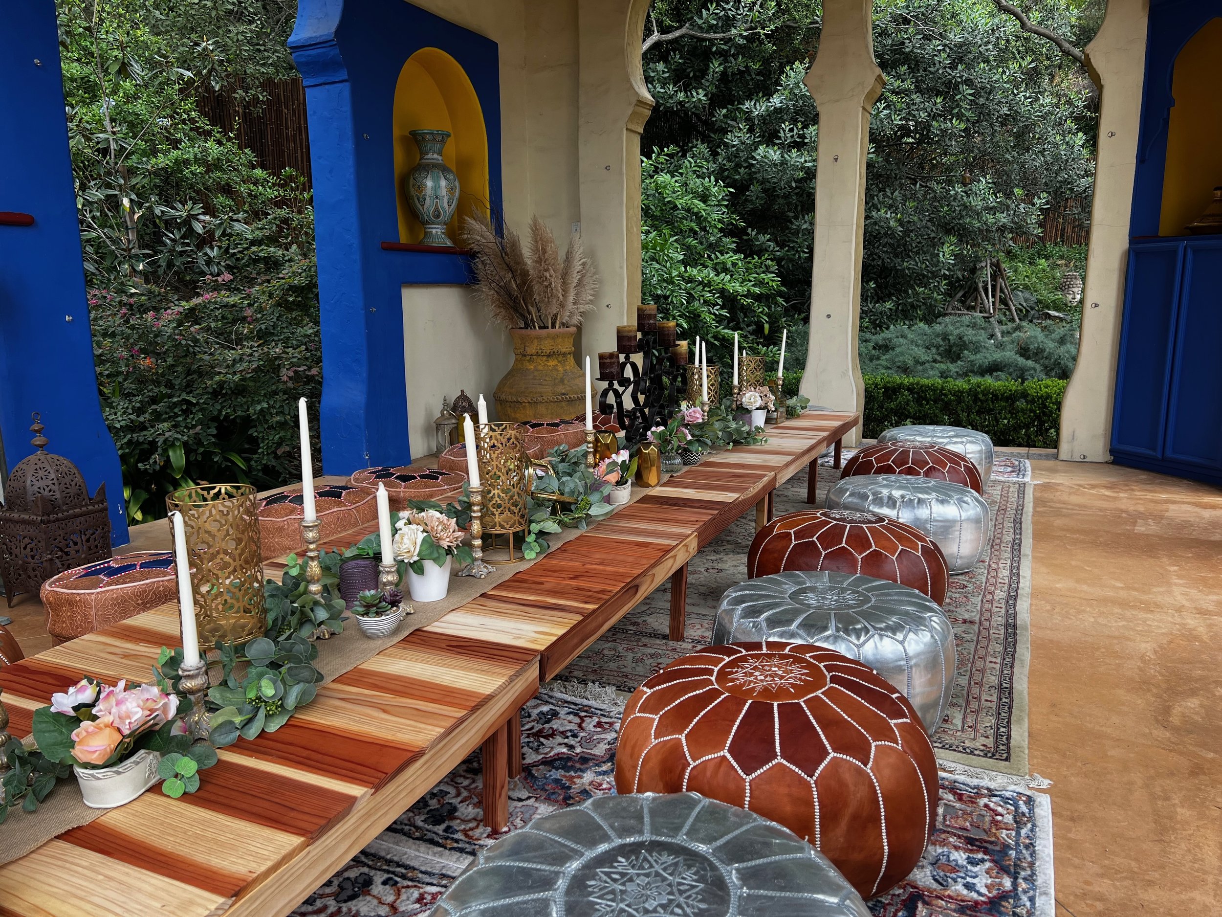 Candle-lined banquet table with leather poufs beside a cobalt-blue Moroccan niche