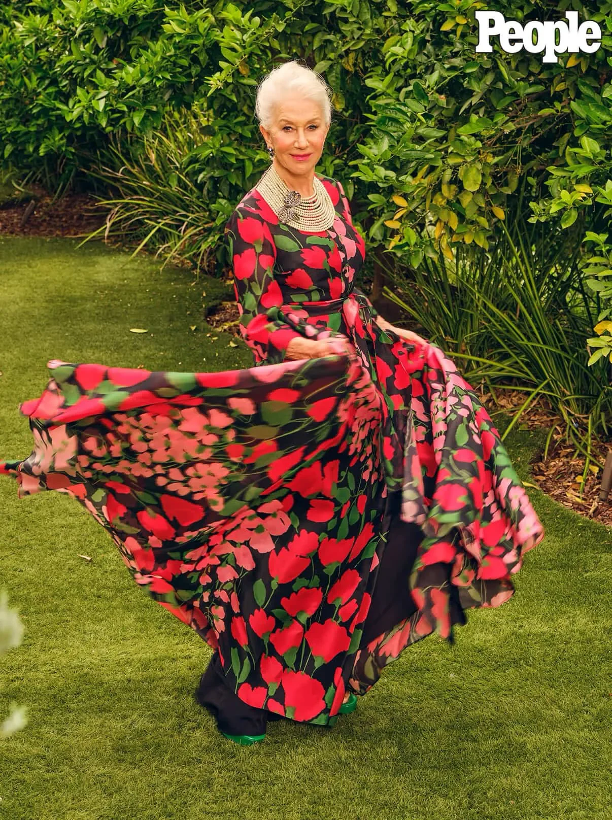 Model twirling in a red floral gown on the sunlit lawn