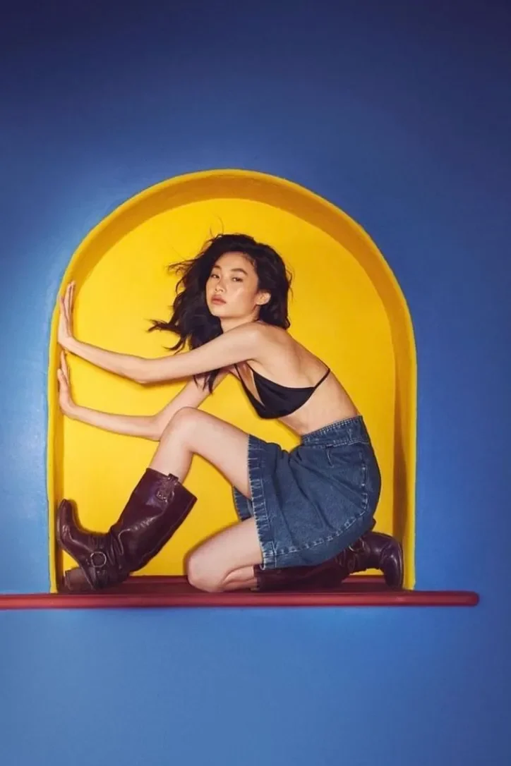 Model posing inside a bright yellow arch in denim and boots