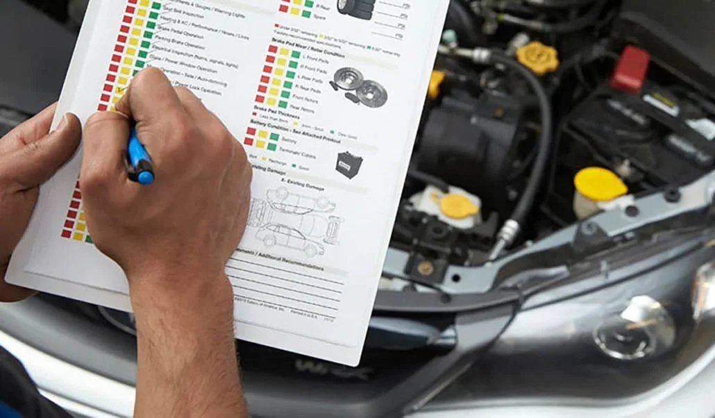 A person is holding a color-coded maintenance or repair checklist with a blue pen, standing in front of an open car hood revealing engine components with yellow caps.