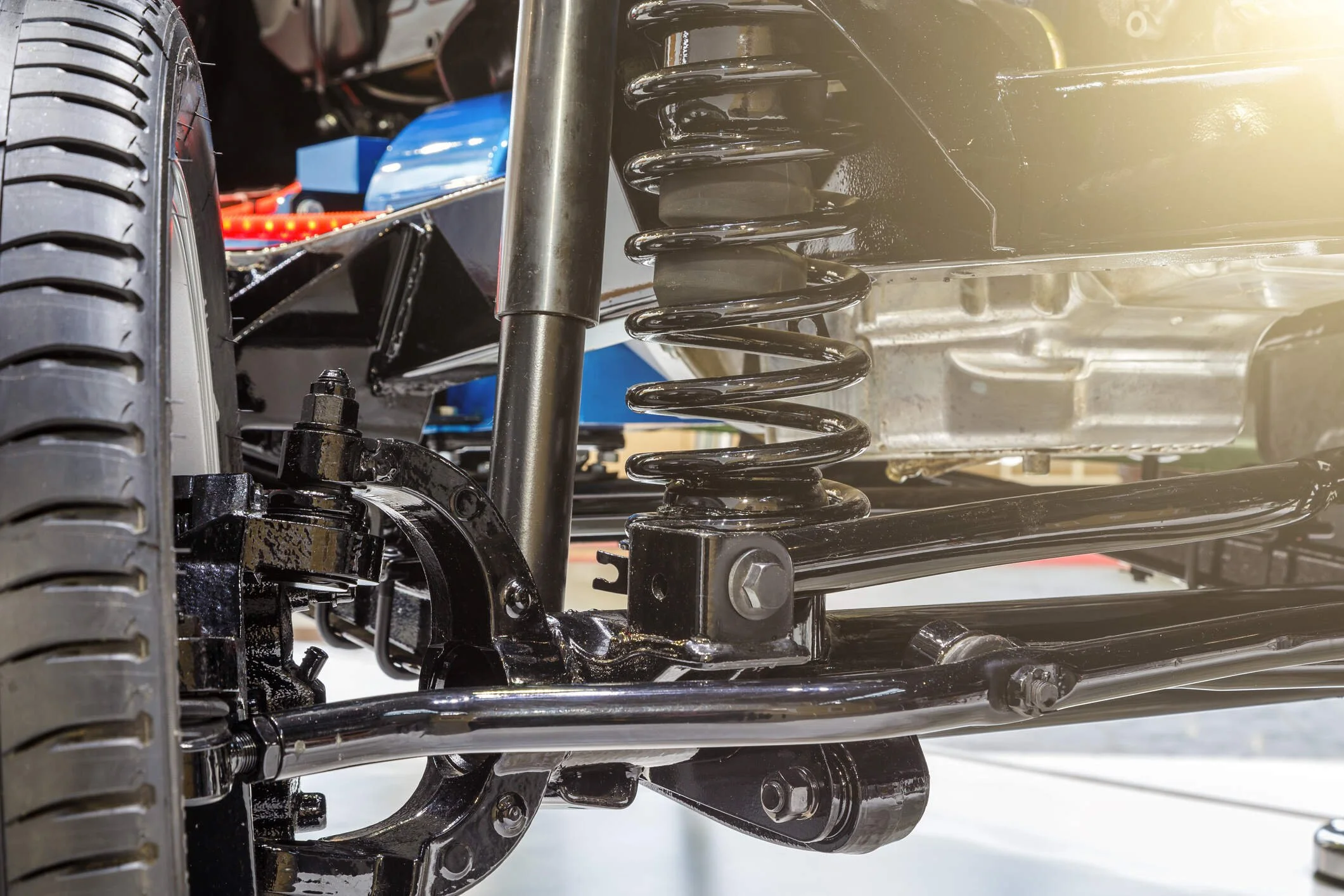 Close-up of a vehicle's suspension system showing a black coil spring, shock absorber, and part of the wheel with tire.