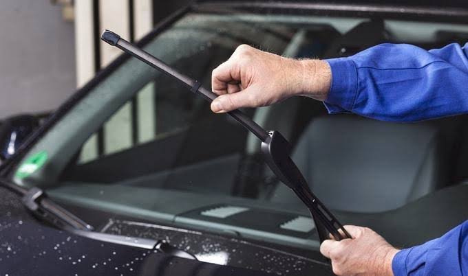 Person cleaning the windshield of a black car using a window squeegee.