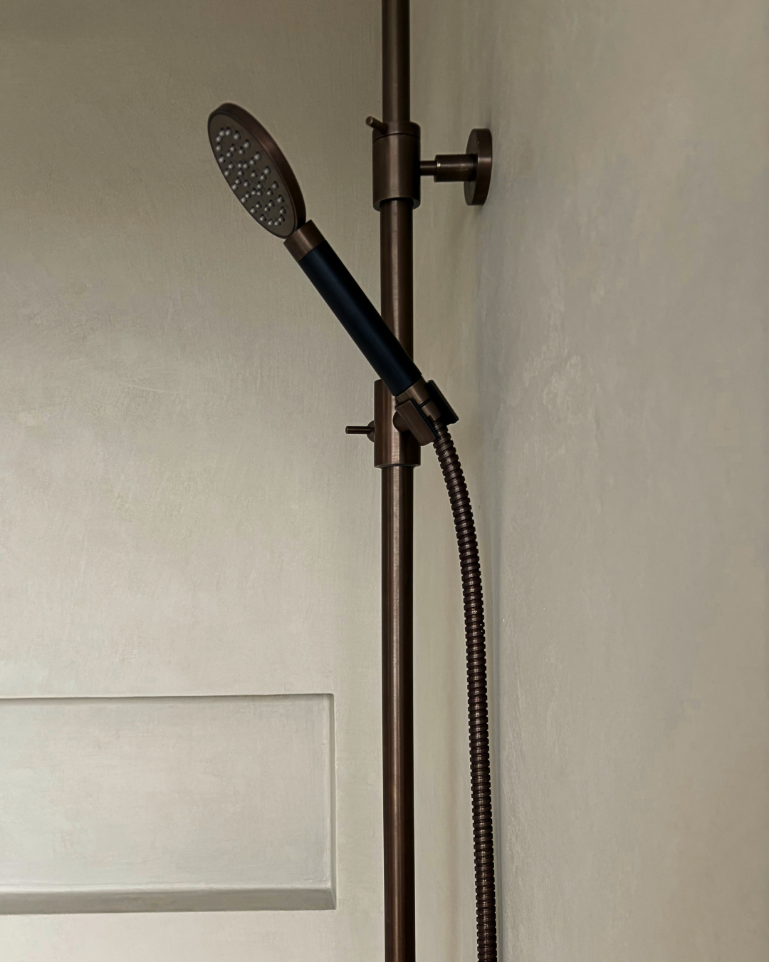 Microcement bathroom wall finish with bronze shower fittings by Surface Revival Auckland.