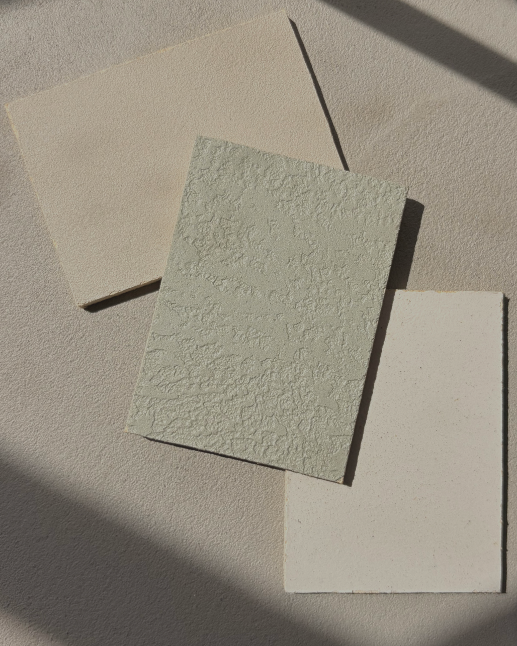 Three microcement sample boards, one with rough surface, one smooth, and one with fine grit.