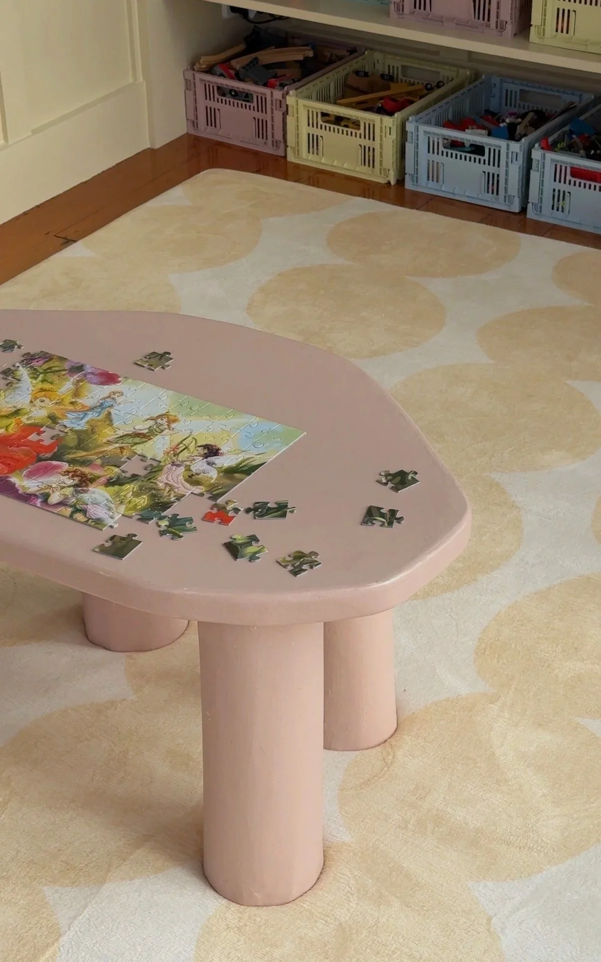 Pink microcement coffee table with rounded edges and cylindrical legs, shown with a jigsaw puzzle on top.