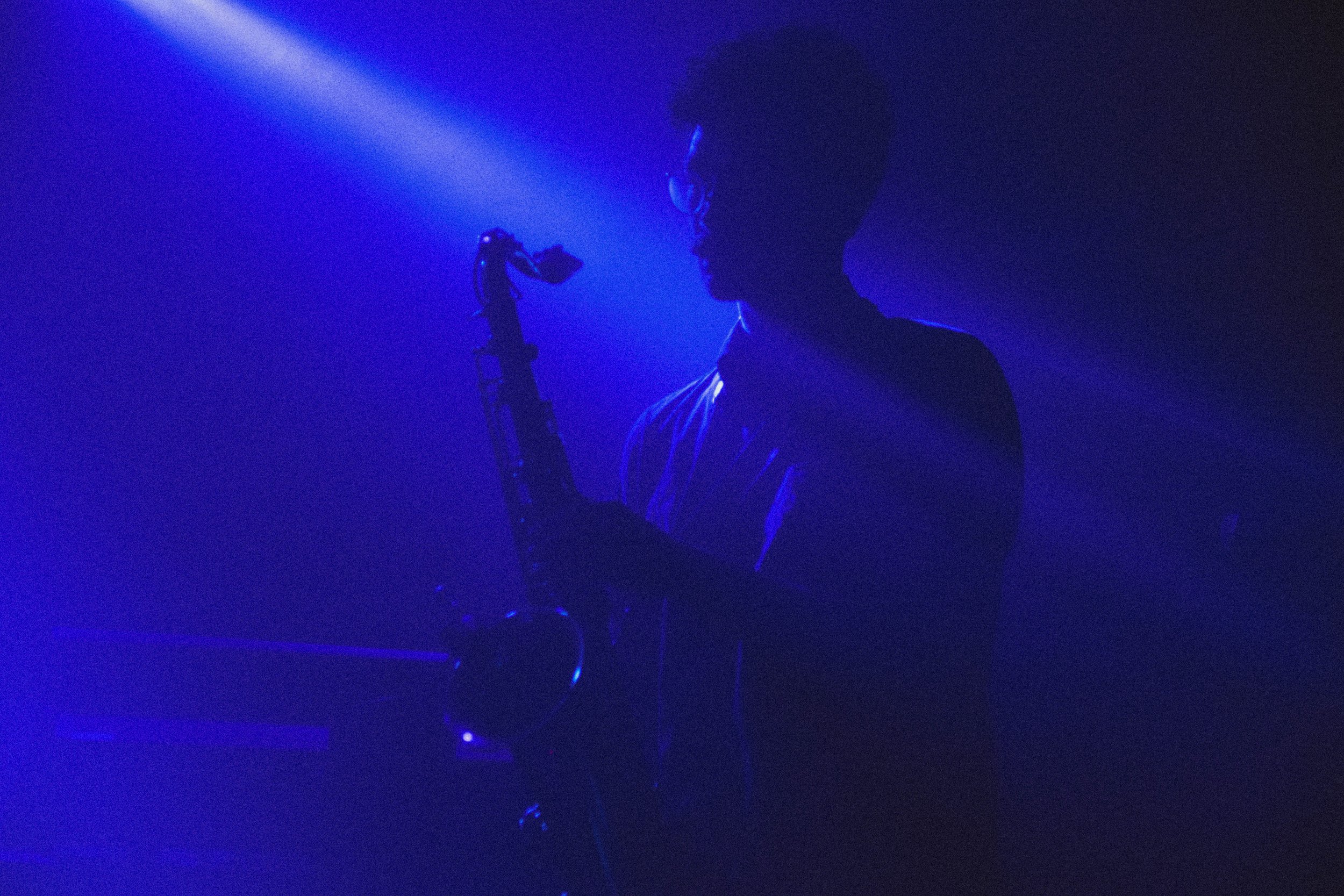 Une personne joue de la guitare dans une ambiance sombre avec un éclairage bleu, créant une atmosphère mystérieuse.
