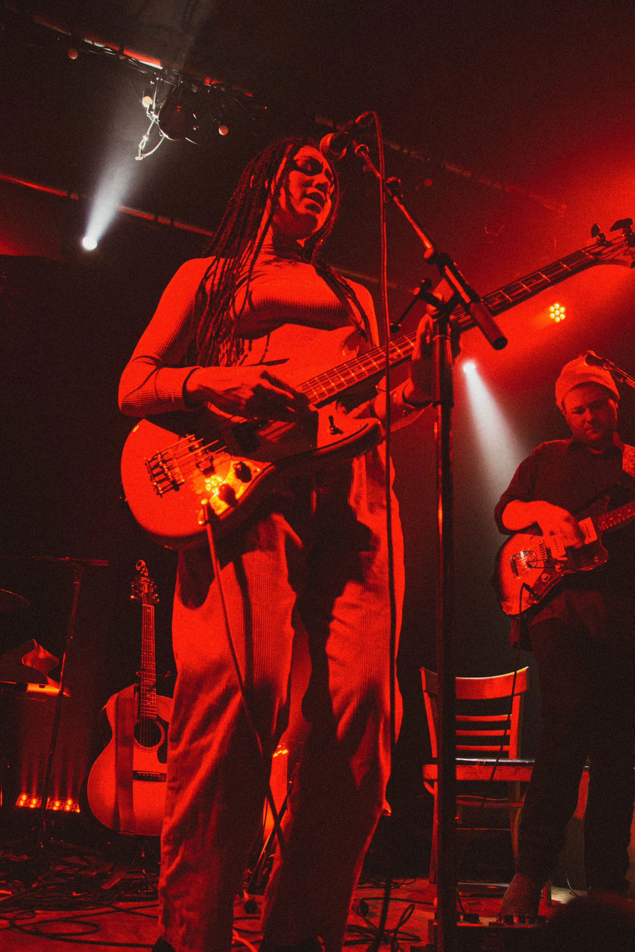 Deux musiciens jouent de la guitare électrique sur scène, sous un éclairage rouge, lors d'un concert.