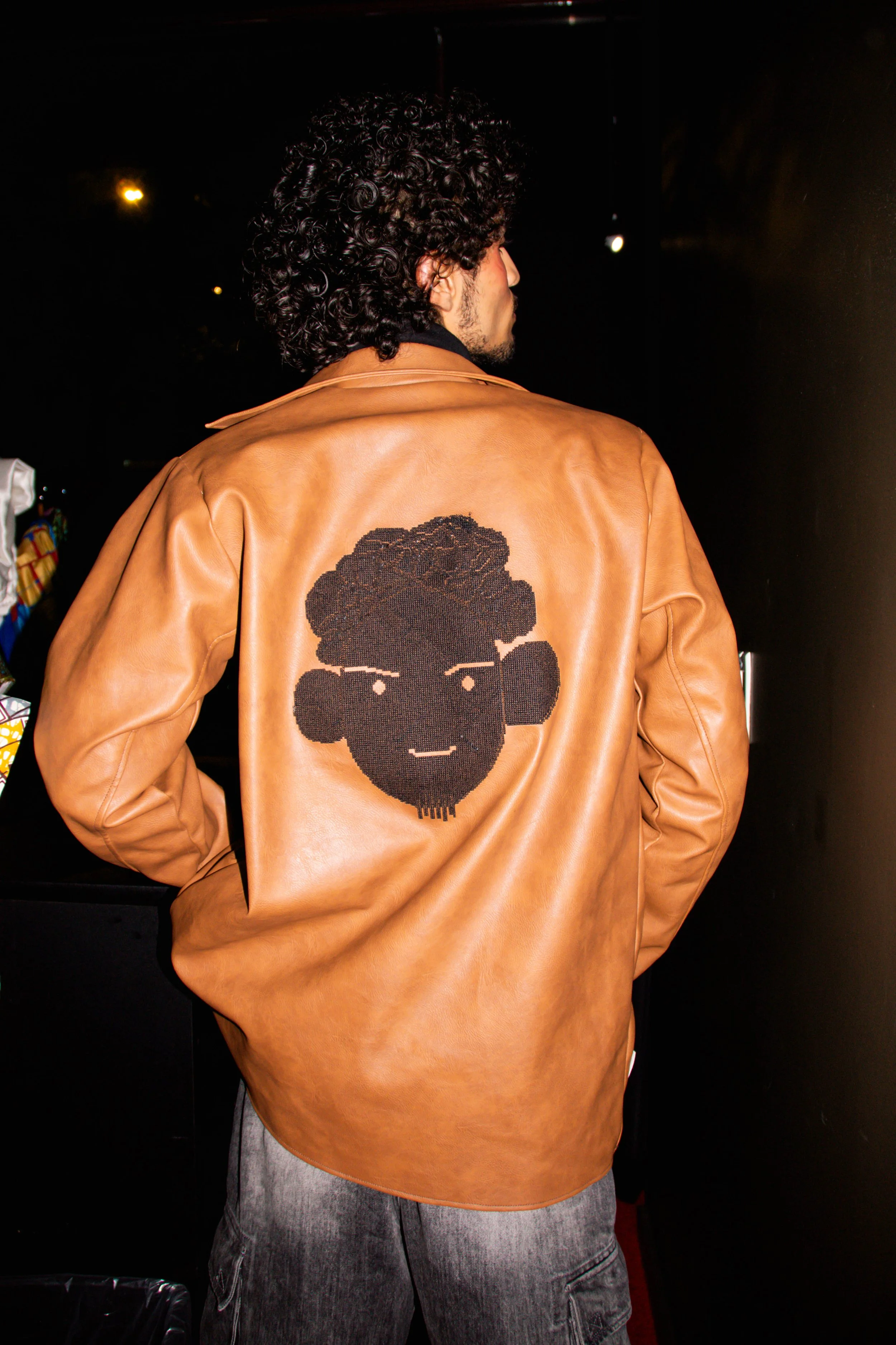 Un homme porte une veste en cuir marron avec un dessin d'un visage stylisé à l'arrière.