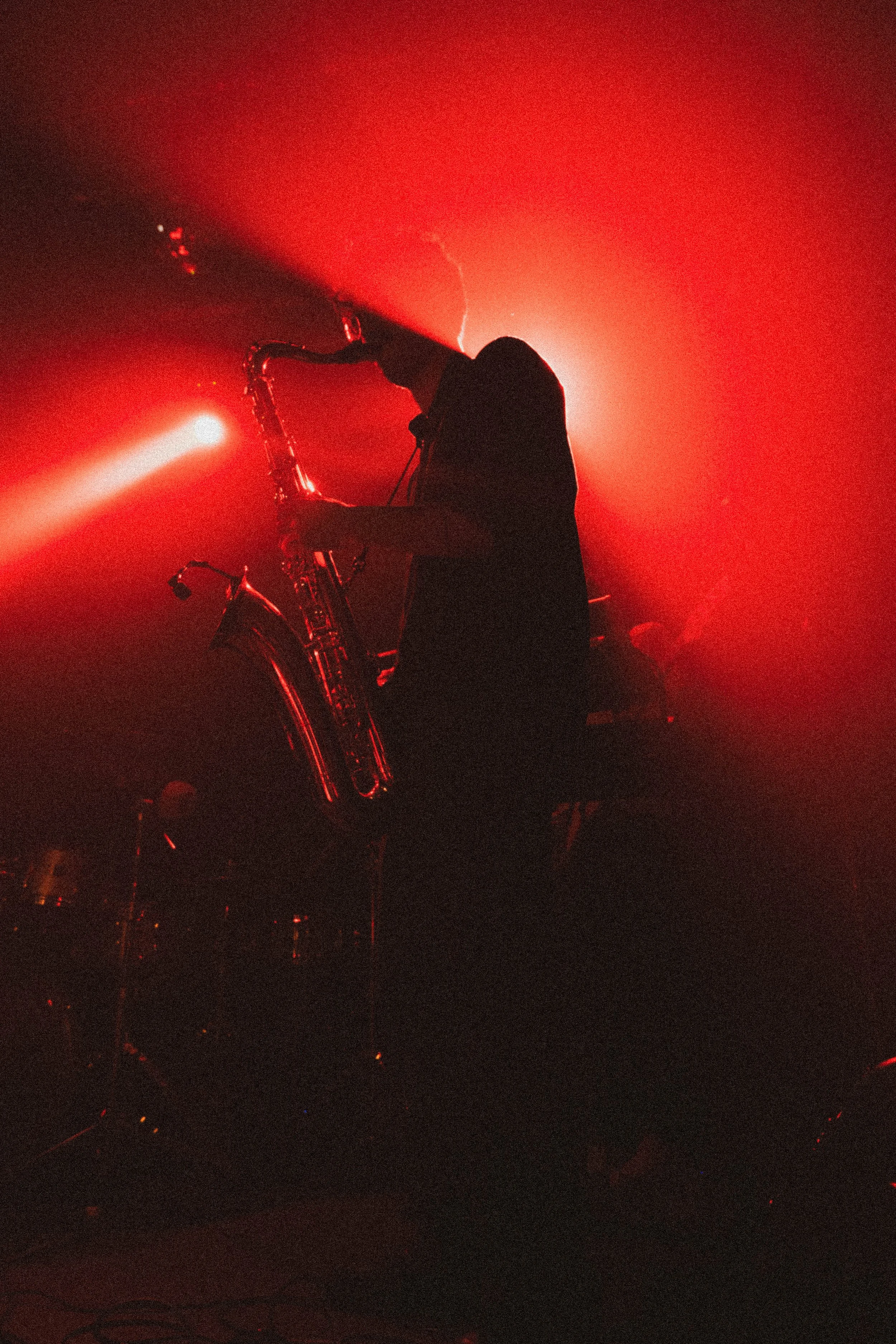 Une silhouette noire d'une personne jouant du saxophone sous des lumières rouge vif et un éclairage dramatique.