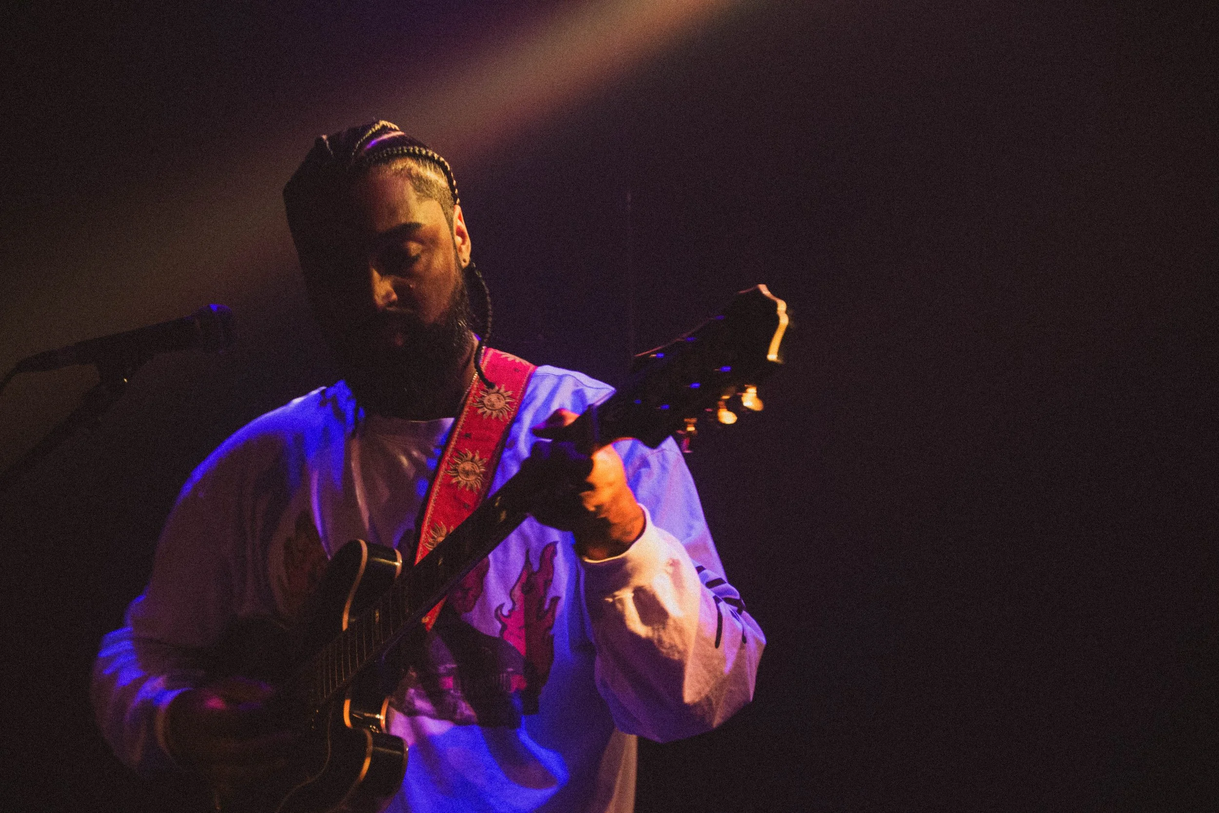 Un homme joue de la guitare lors d'une performance sur scène, avec un éclairage tamisé et une ambiance sombre.