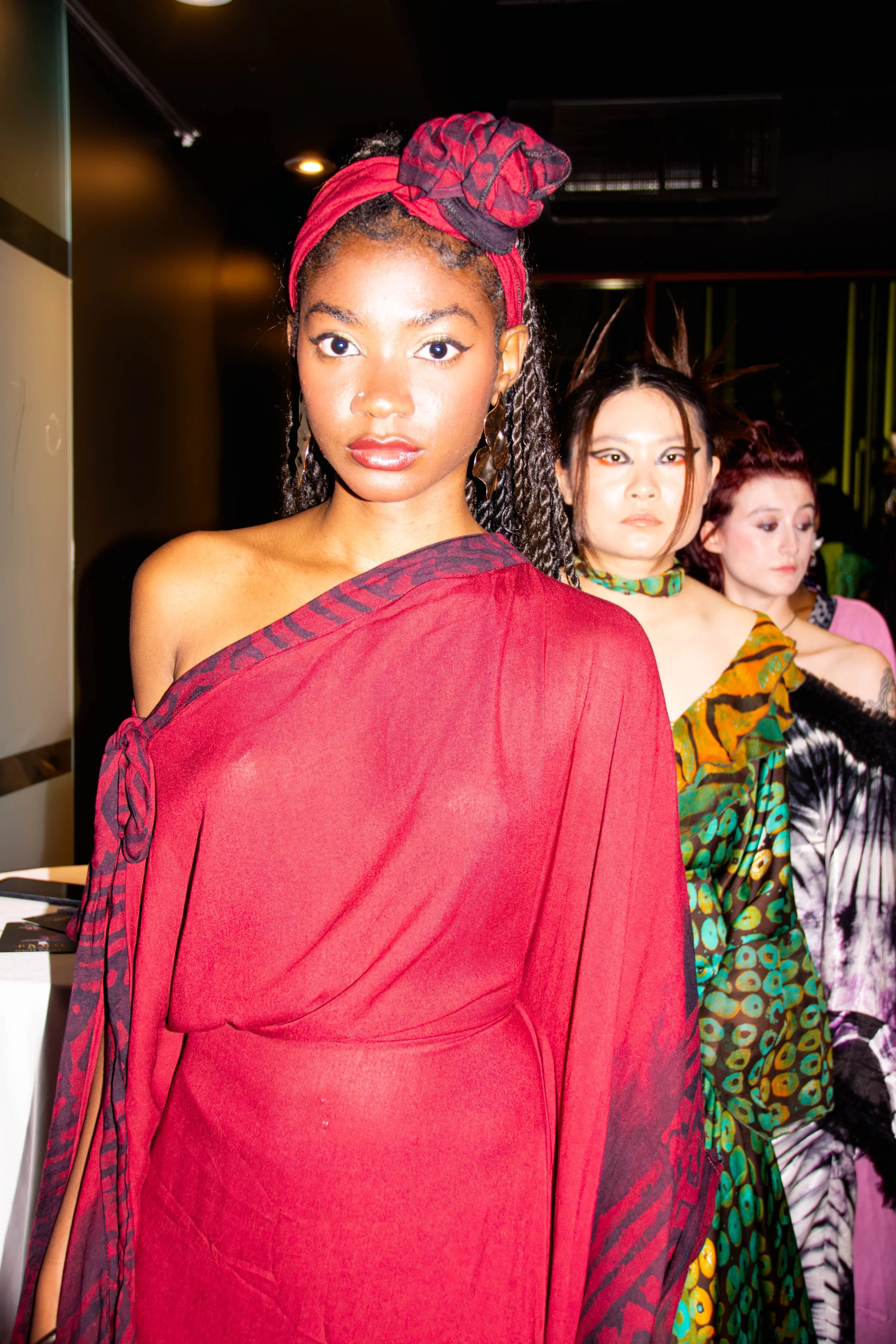 Trois femmes posent lors d'un événement de mode, portant des tenues colorées et audacieuses dans un décor intérieur.