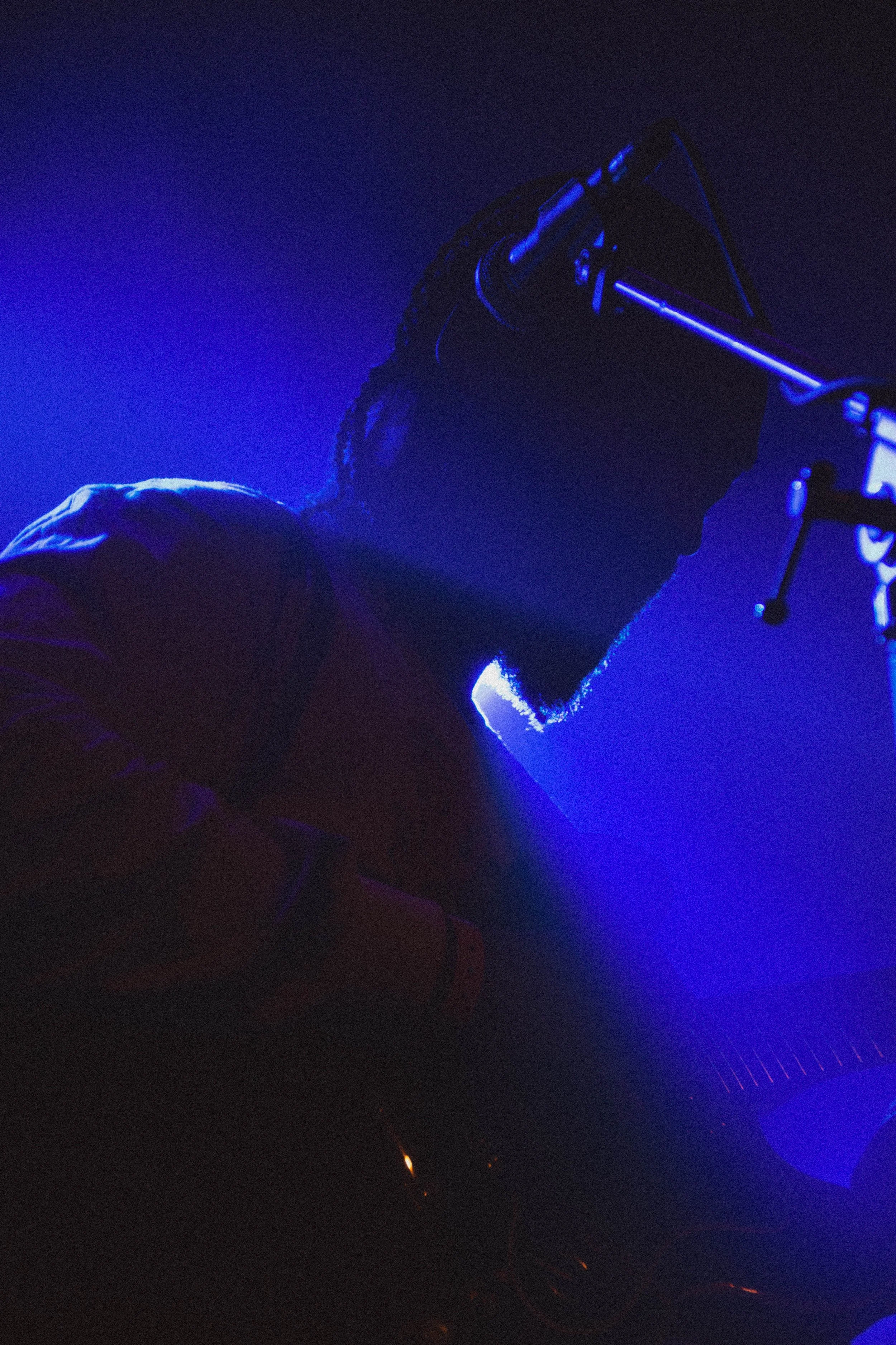 Silhouette d'un DJ ou musicien dans une lumière bleue, portant des casques, jouant ou mixant de la musique dans une atmosphère sombre.