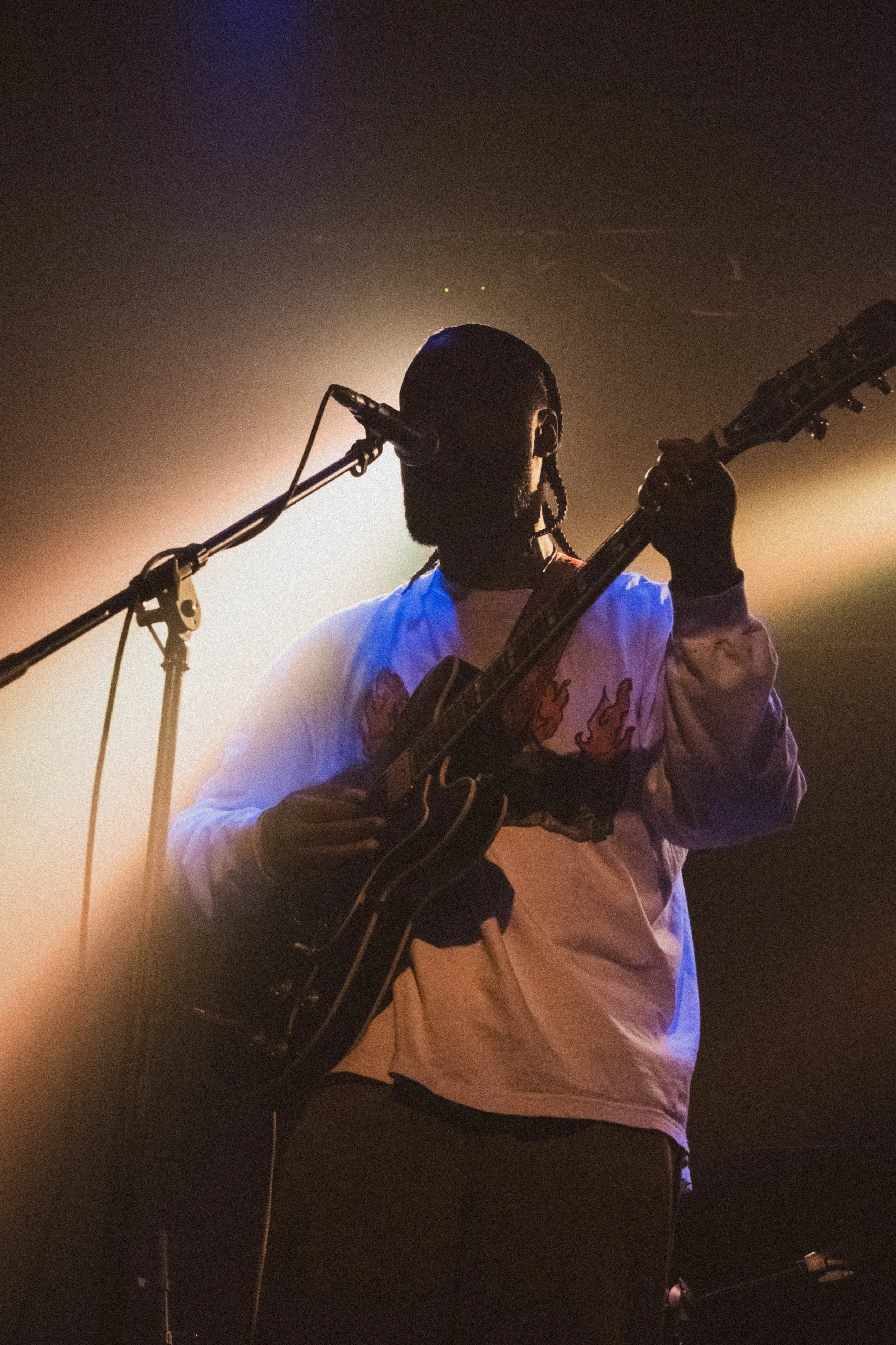 Musicien jouant de la guitare sur scène avec un micro, éclairage de scène en arrière-plan.