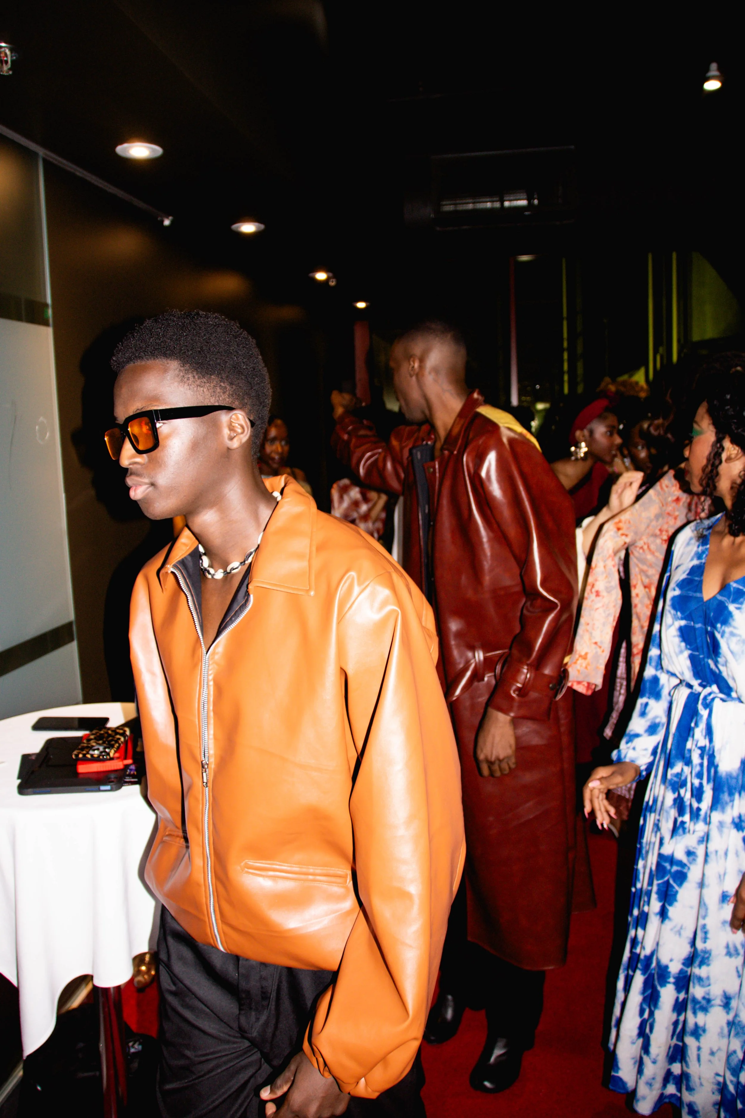 Groupe de personnes à une fête ou un événement, avec des vêtements colorés et tendance, dans un espace intérieur avec éclairage tamisé.
