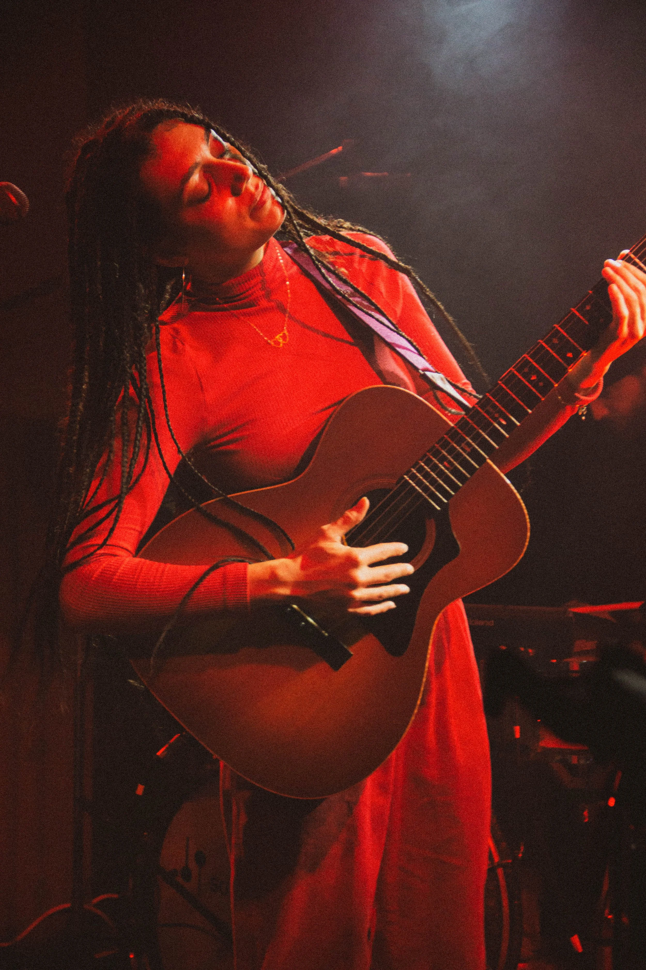 Une femme jouant de la guitare électrique lors d'une performance, sous un éclairage rouge.