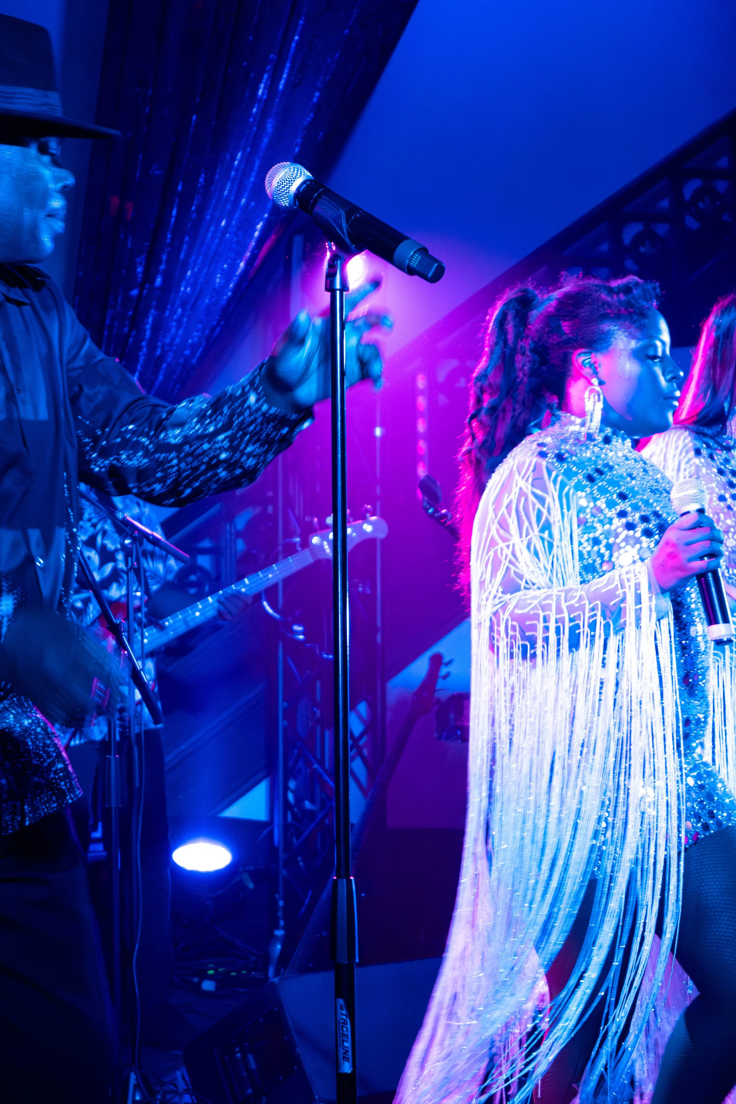 Performers en costumes scintillants sur scène lors d'un concert avec éclairage violet et bleu.