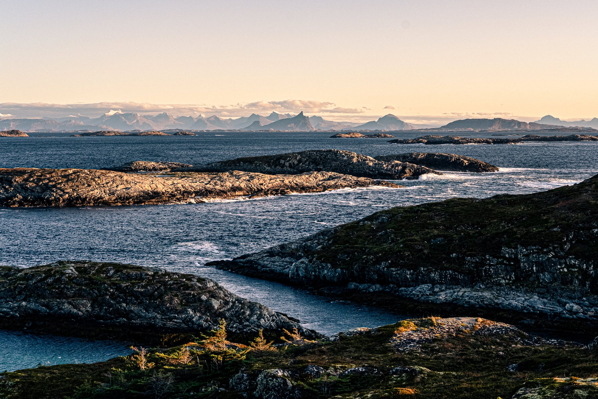 Scenic view of rocky islands and mountains in the background with calm water and a clear sky.